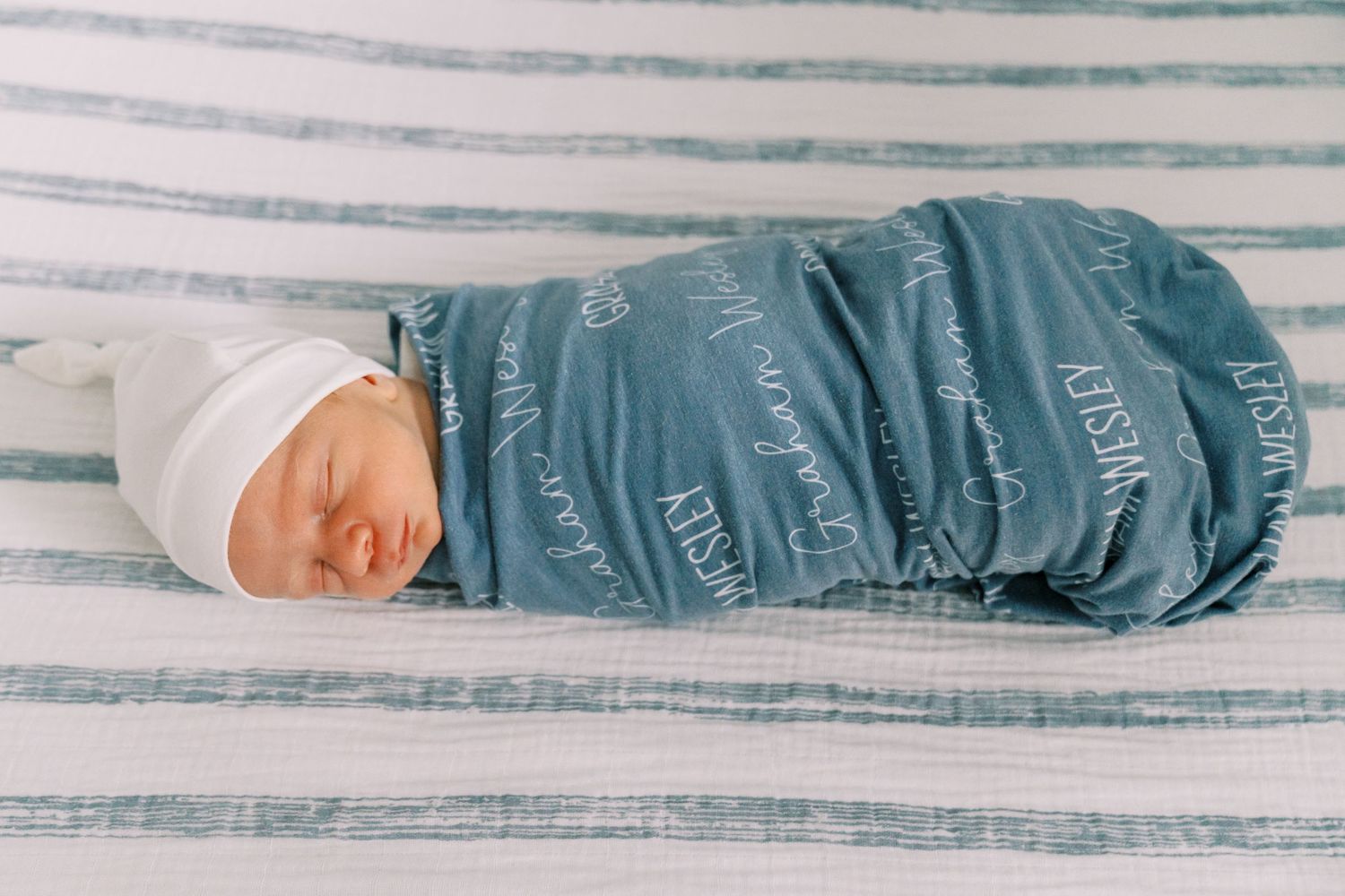 Newborn baby sleeping peacefully in blue and white striped swaddle.