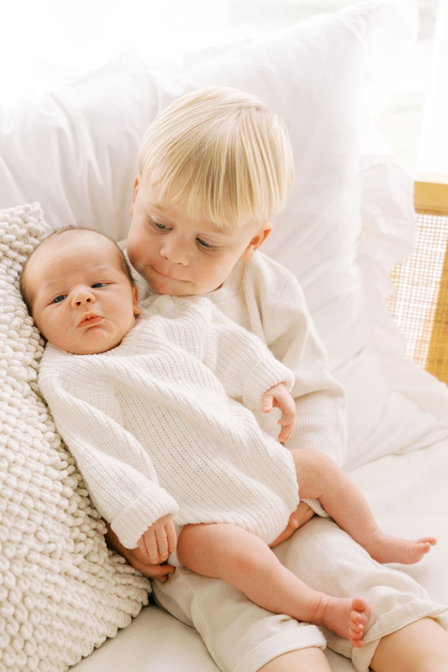 Two children in white clothing lying together on textured white bedding.