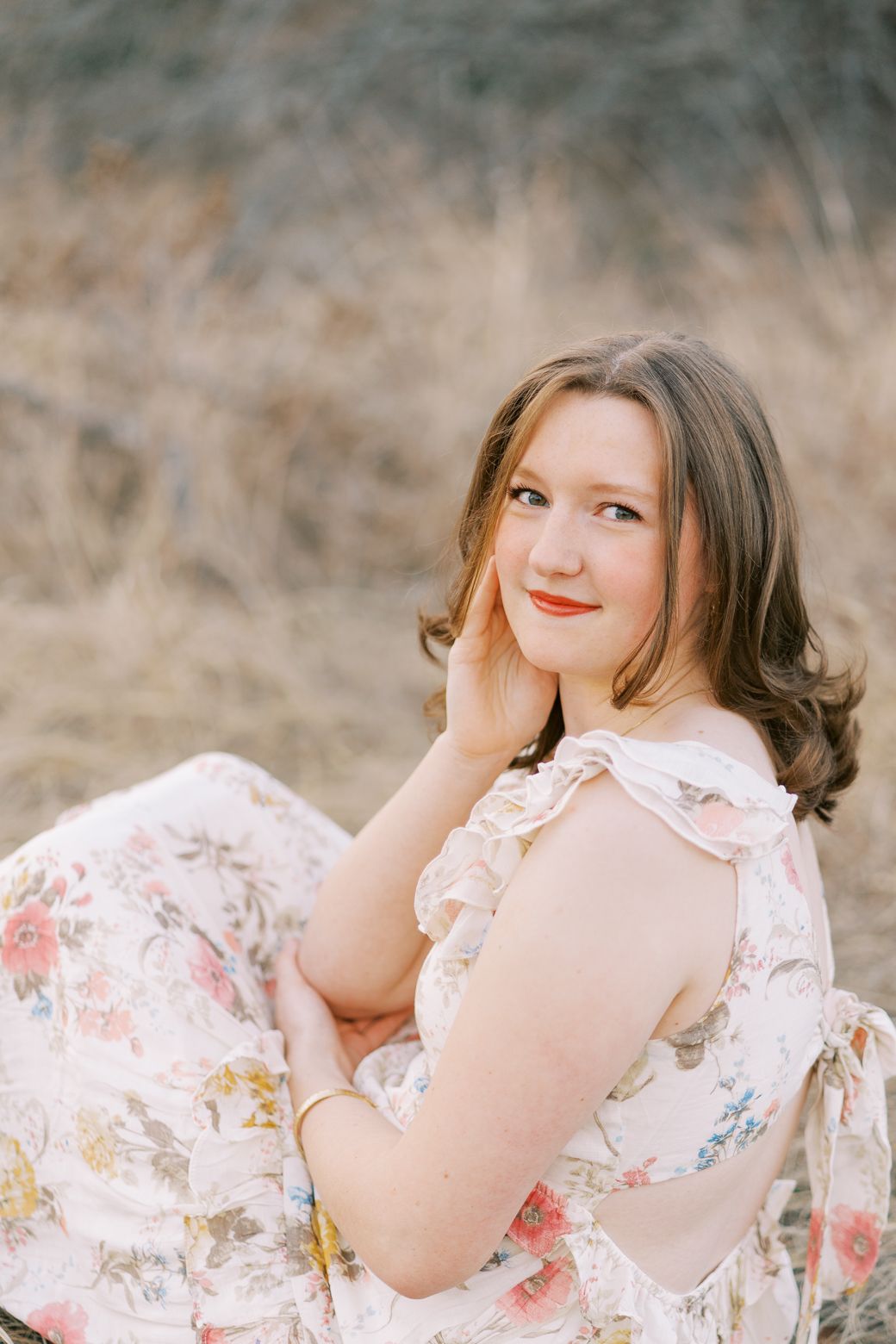 A dreamy outdoor portrait in a floral dress with soft natural lighting and blurred field background.
