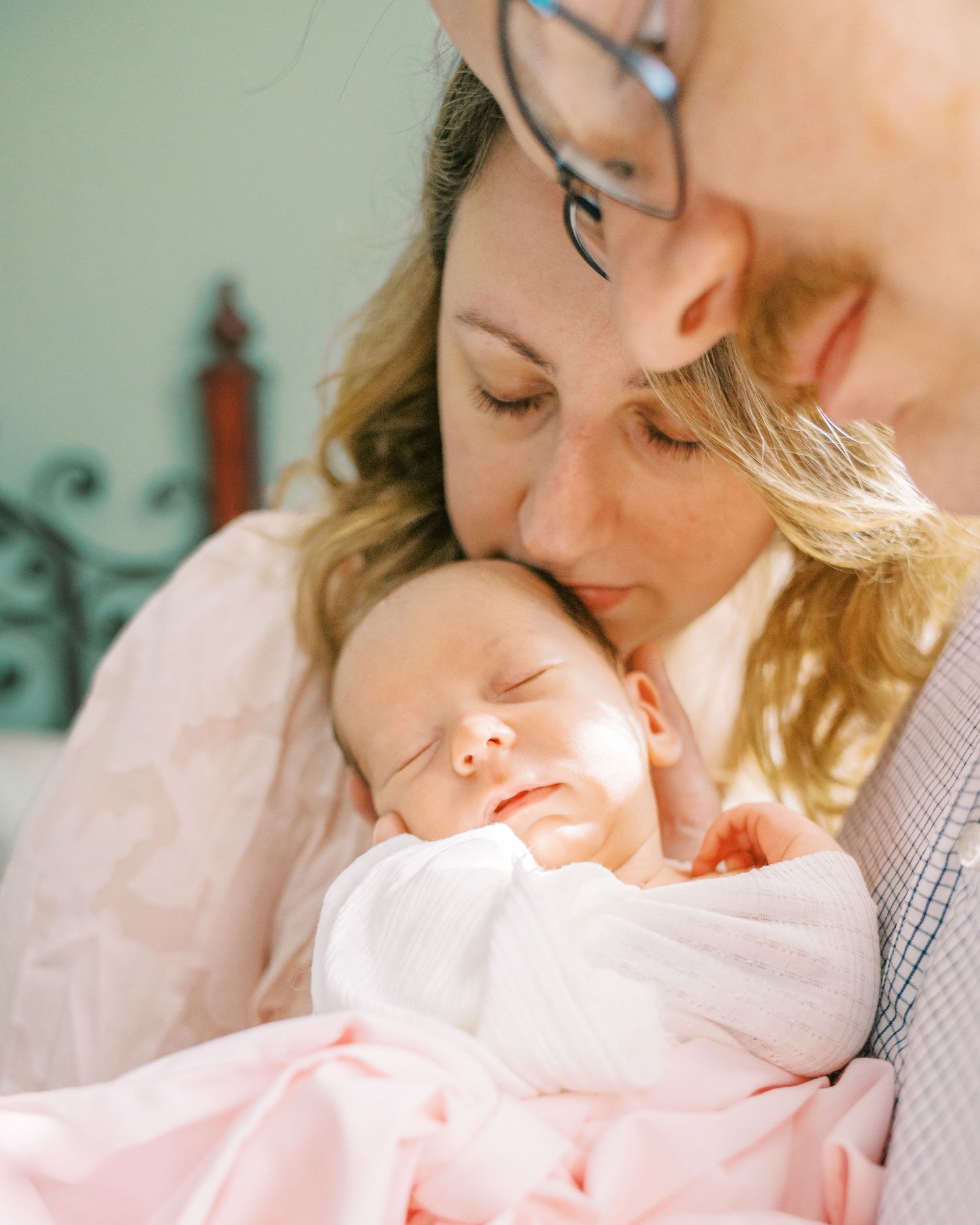 Two parents lovingly cradle their sleeping newborn baby wrapped in a soft pink blanket.