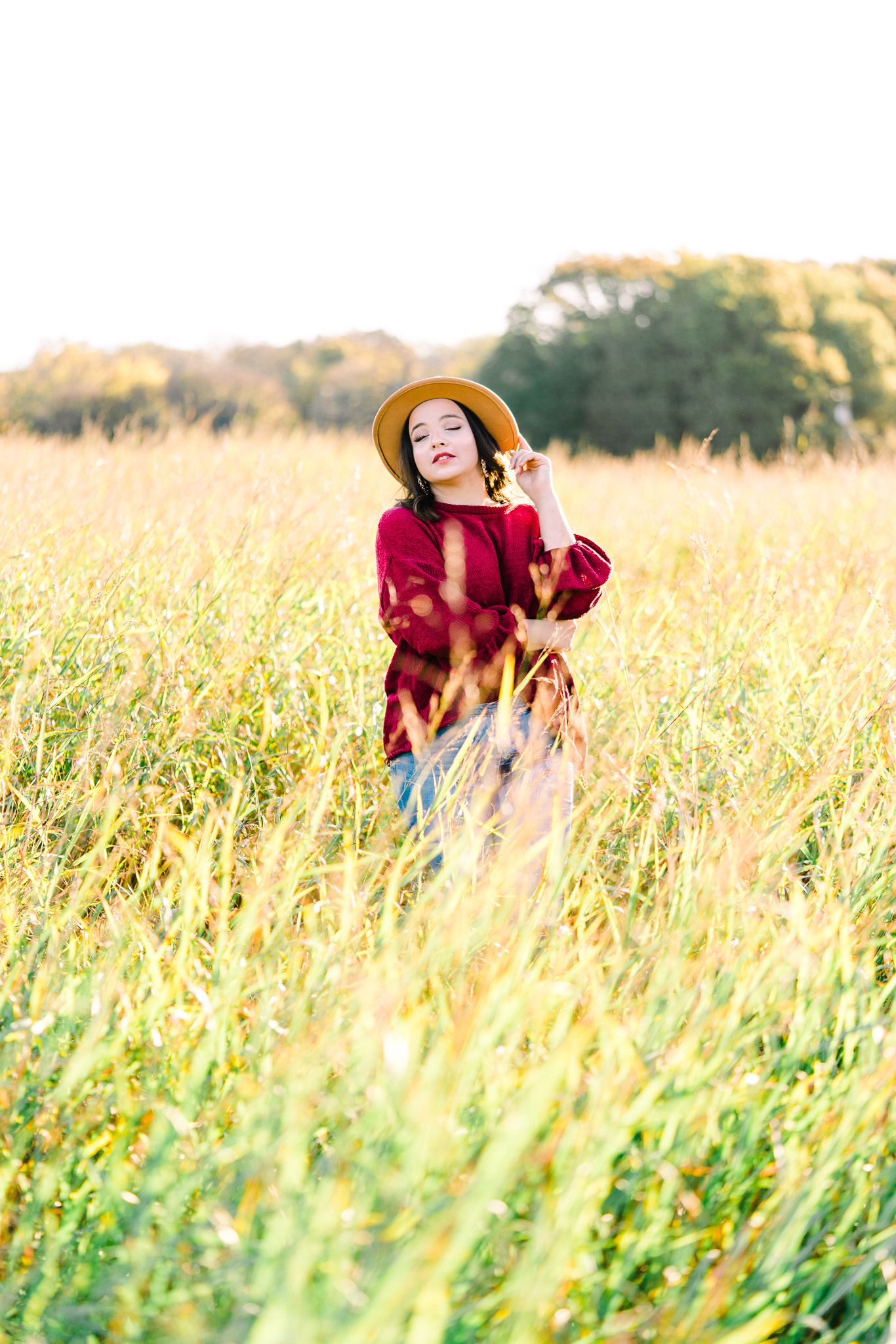 Person in red sweater dancing playfully in a sunlit meadow with tall golden grass.