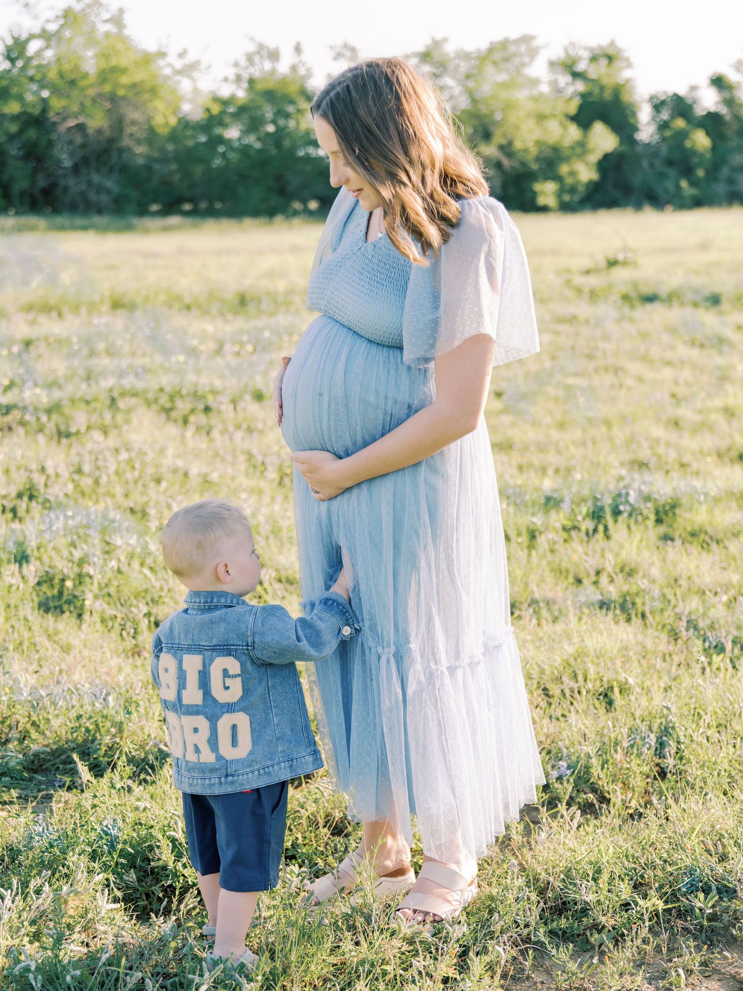 A tender family moment captured in a sunlit field with soft natural lighting and flowing dresses.