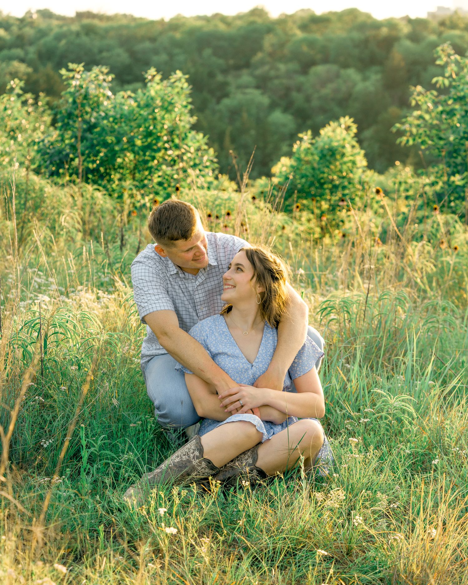 A couple shares intimate moments together in a sunlit meadow with tall grass and greenery.