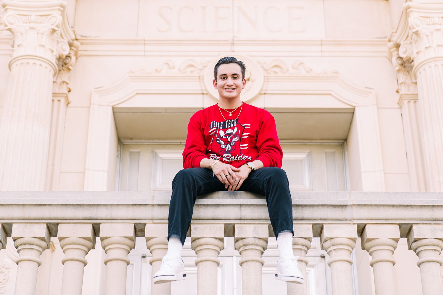 A person wearing a red sweatshirt sits on ornate white stone architecture with decorative columns and molding.