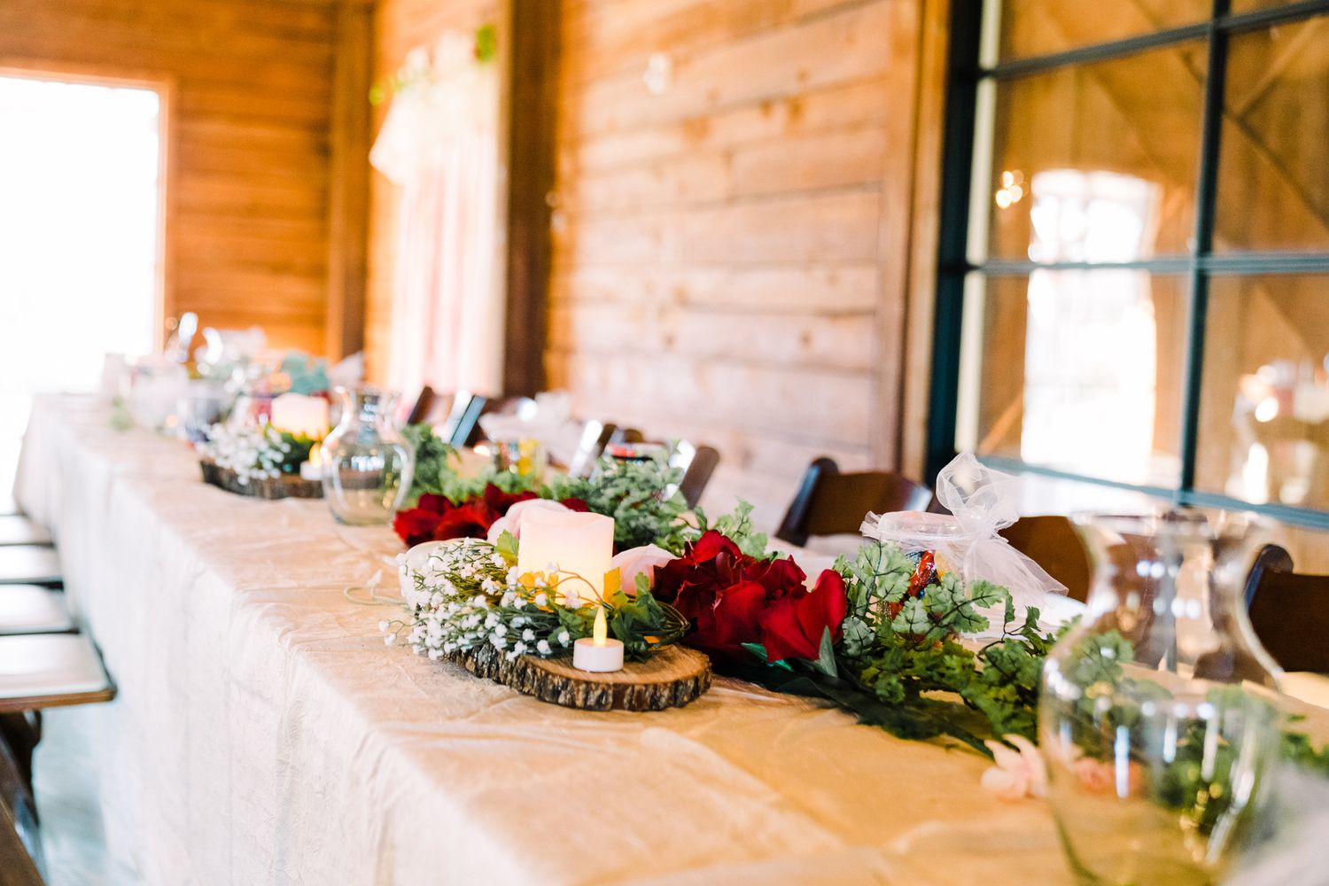 Long wooden table decorated with romantic floral centerpieces and candles for a rustic wedding reception.