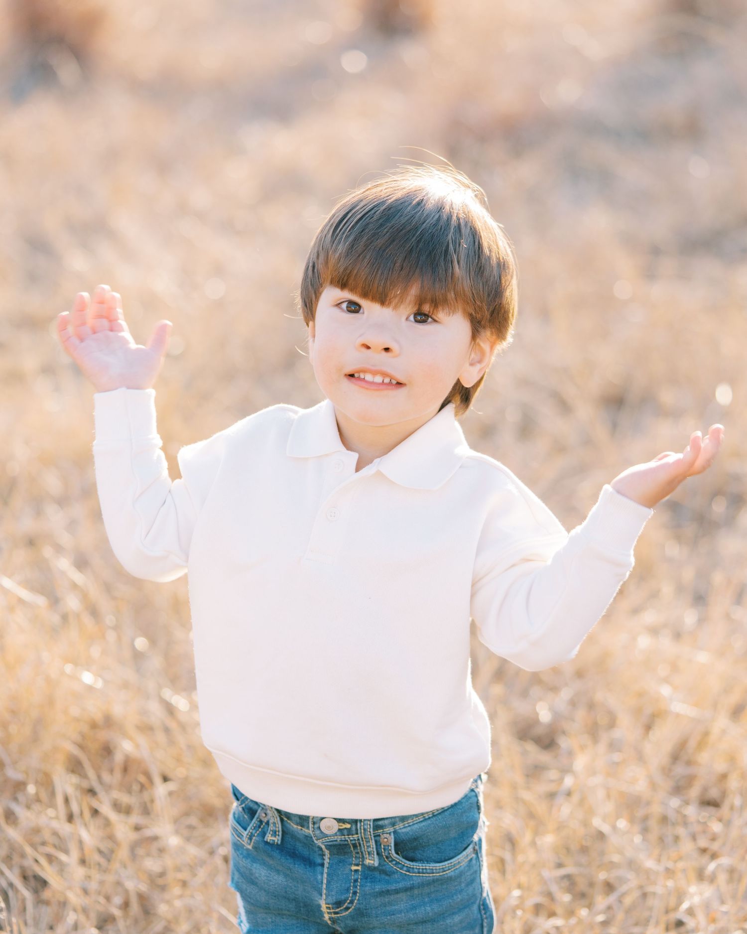 A young child in a white sweater and jeans plays joyfully in a golden field during sunset.