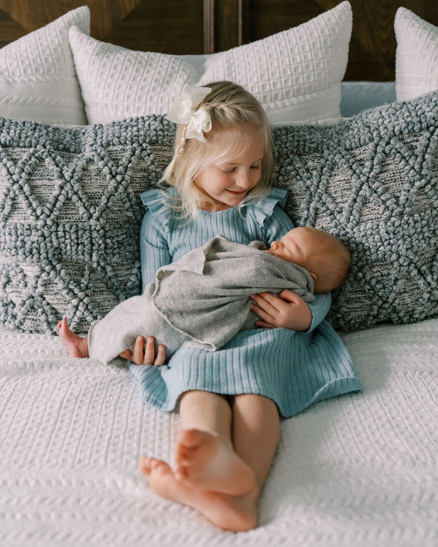 A sweet sibling moment on a bed with blue patterned pillows and white bedding.