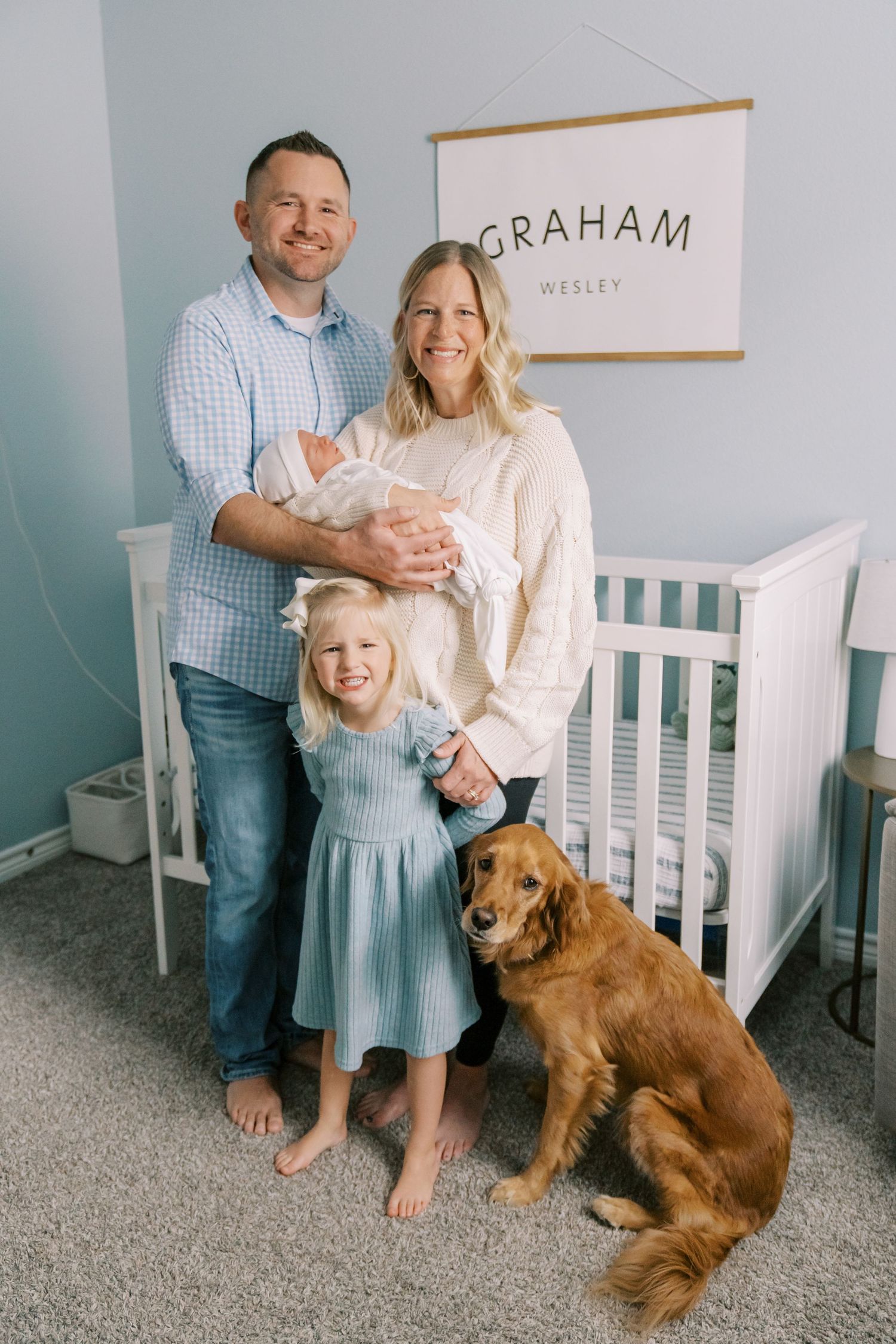 Family portrait in nursery with golden retriever and newborn baby.
