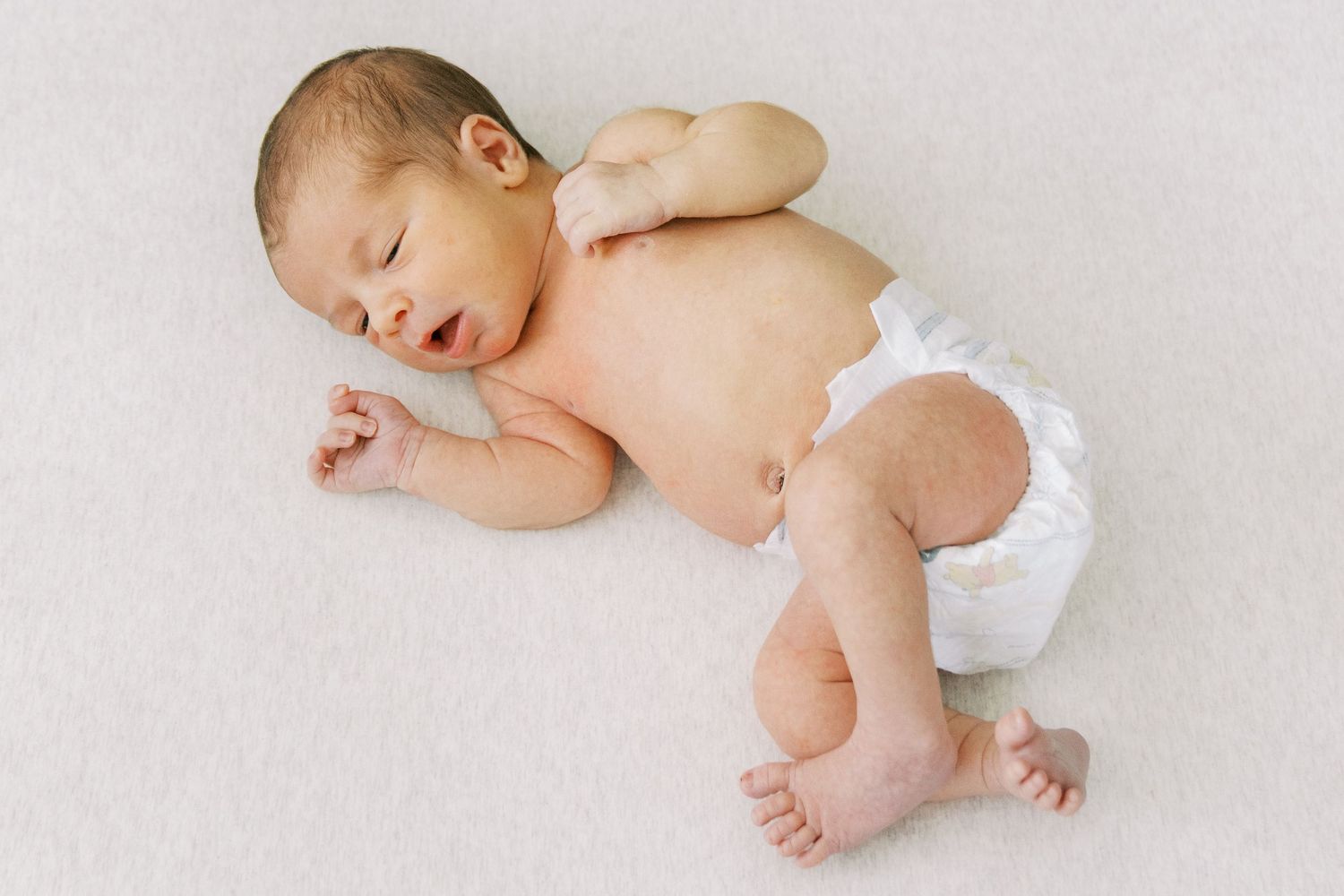 Sleeping newborn baby in white diaper lying on soft white blanket in different peaceful resting positions.