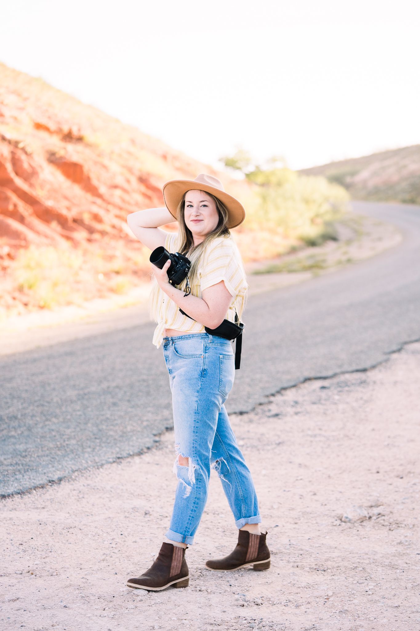 A photography session on a desert trail with someone wearing western-inspired attire and holding a camera.