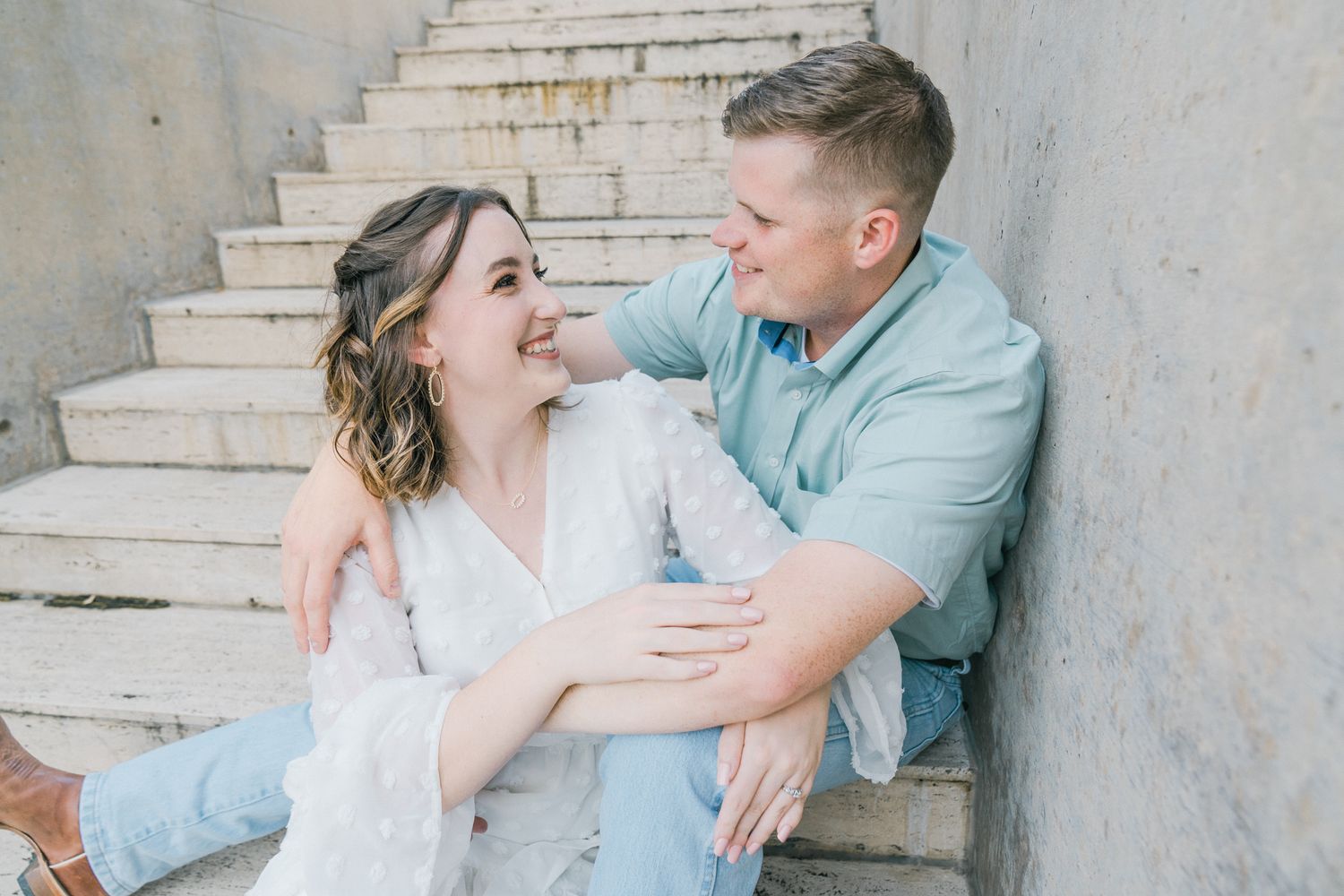 A couple in casual attire sitting together on concrete steps during a romantic photoshoot.