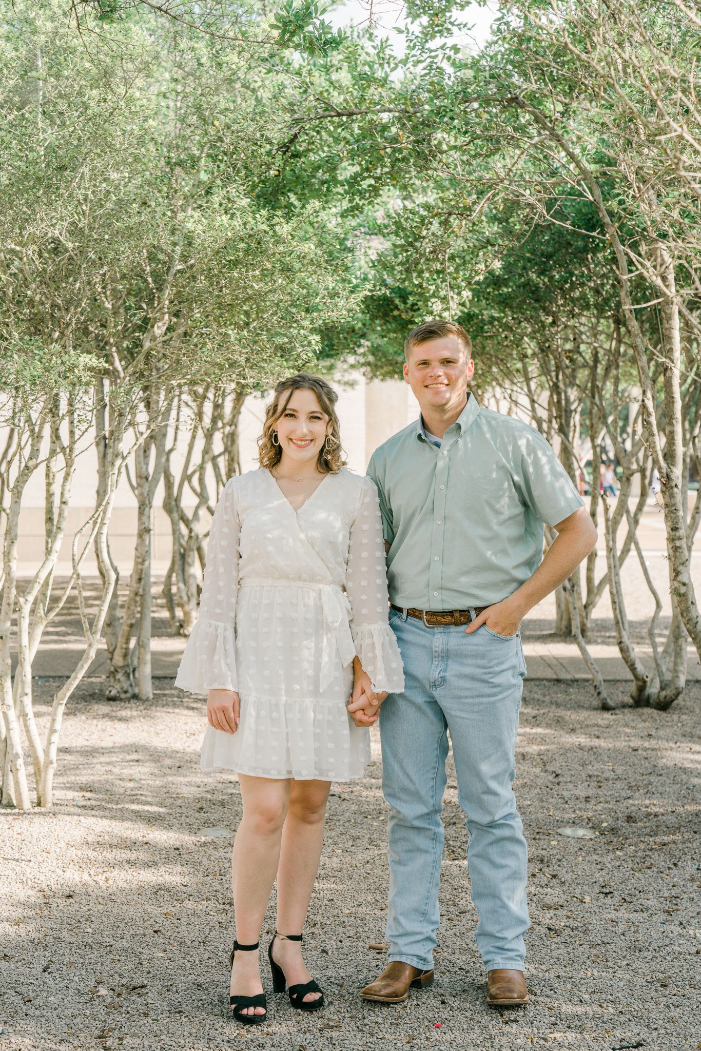 A couple poses together in a wooded area wearing coordinating light blue and white outfits.