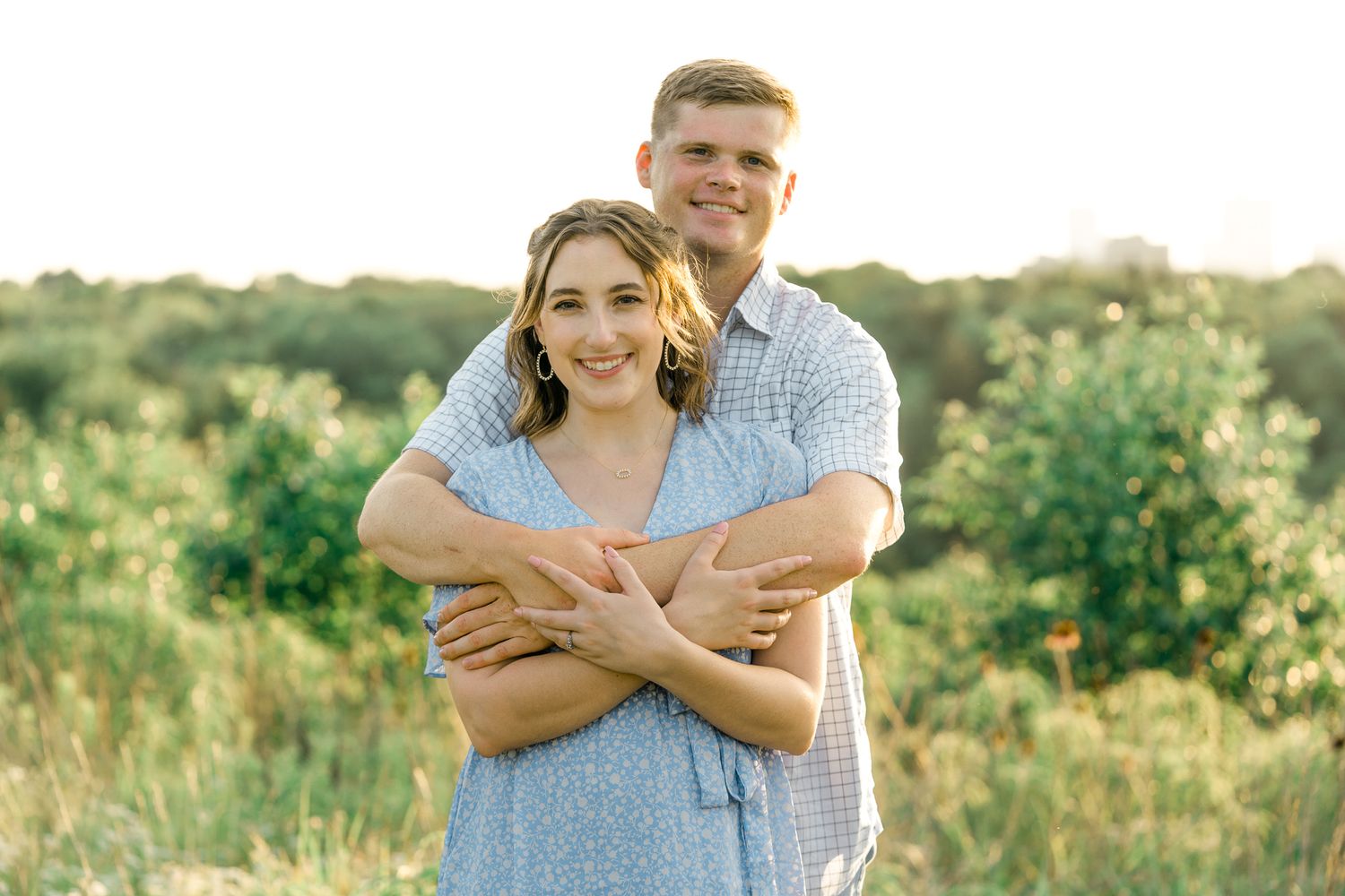 Romantic outdoor photoshoot with couple wearing blue and white against natural meadow backdrop.