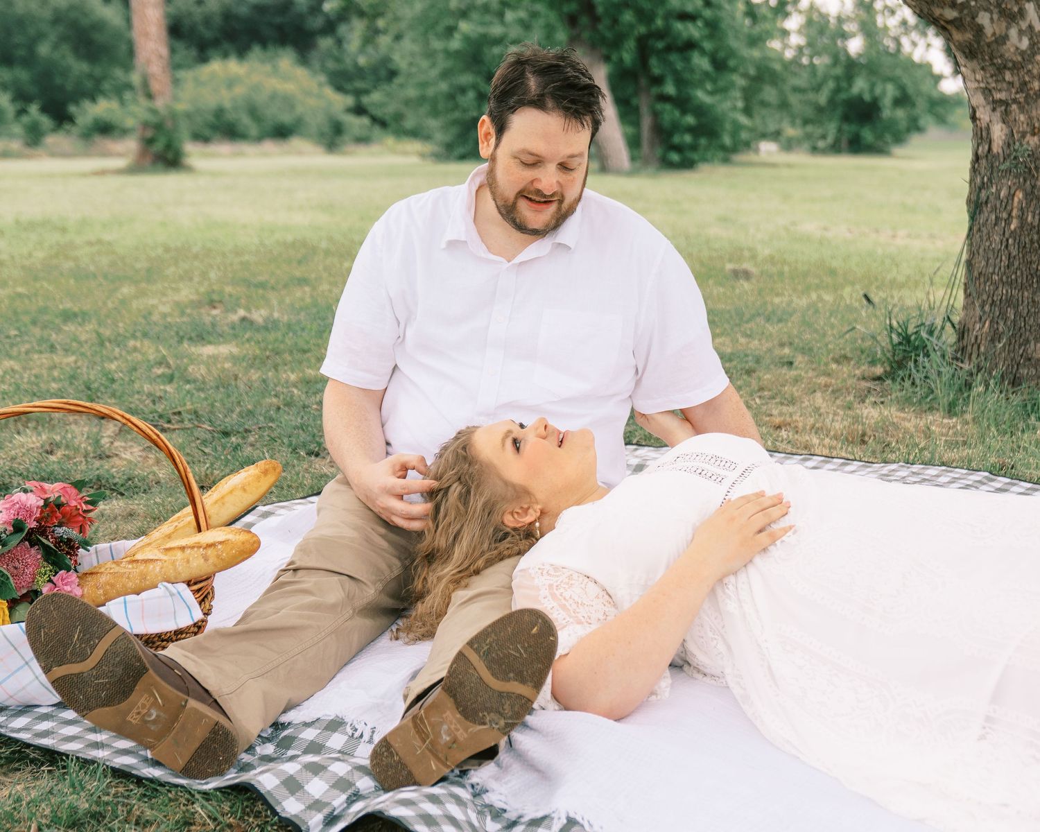 Couple enjoying a romantic picnic on a blanket in a park, with a basket of bread and flowers nearby.