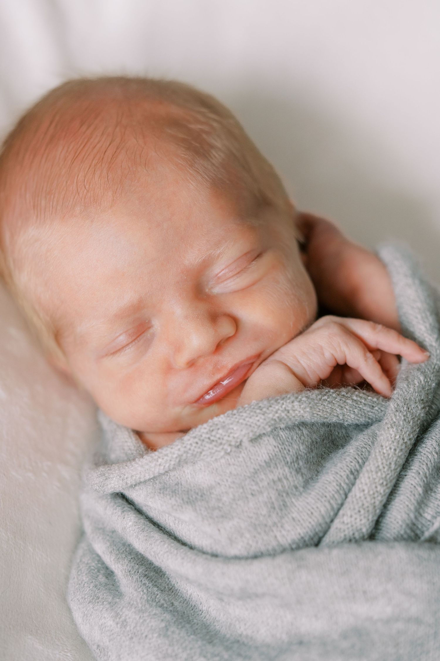 Sleeping newborn baby wrapped in soft gray blanket shown in series of peaceful close-up shots.