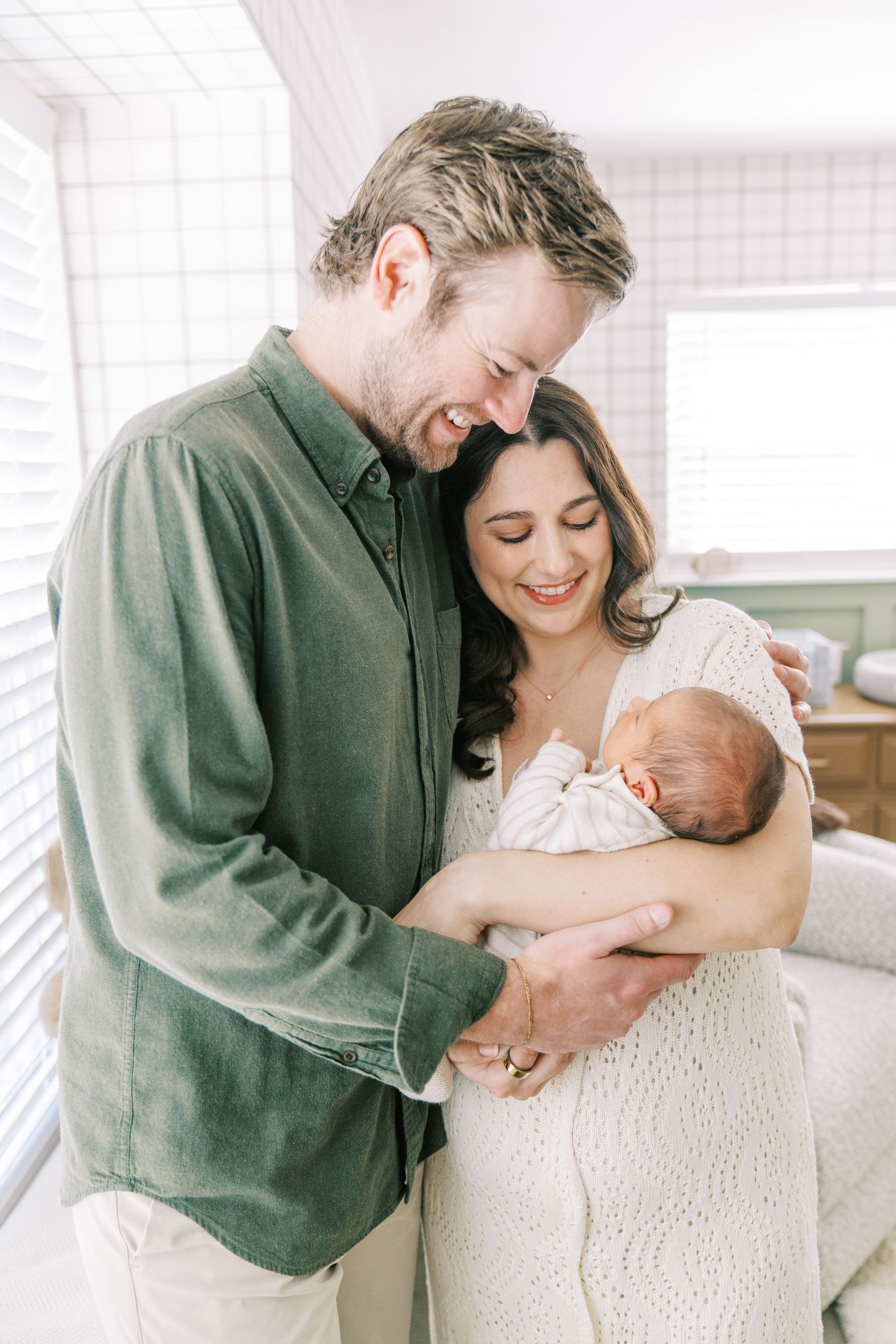 A couple shares tender moments with their newborn baby in a bright white room, captured in three intimate photos.