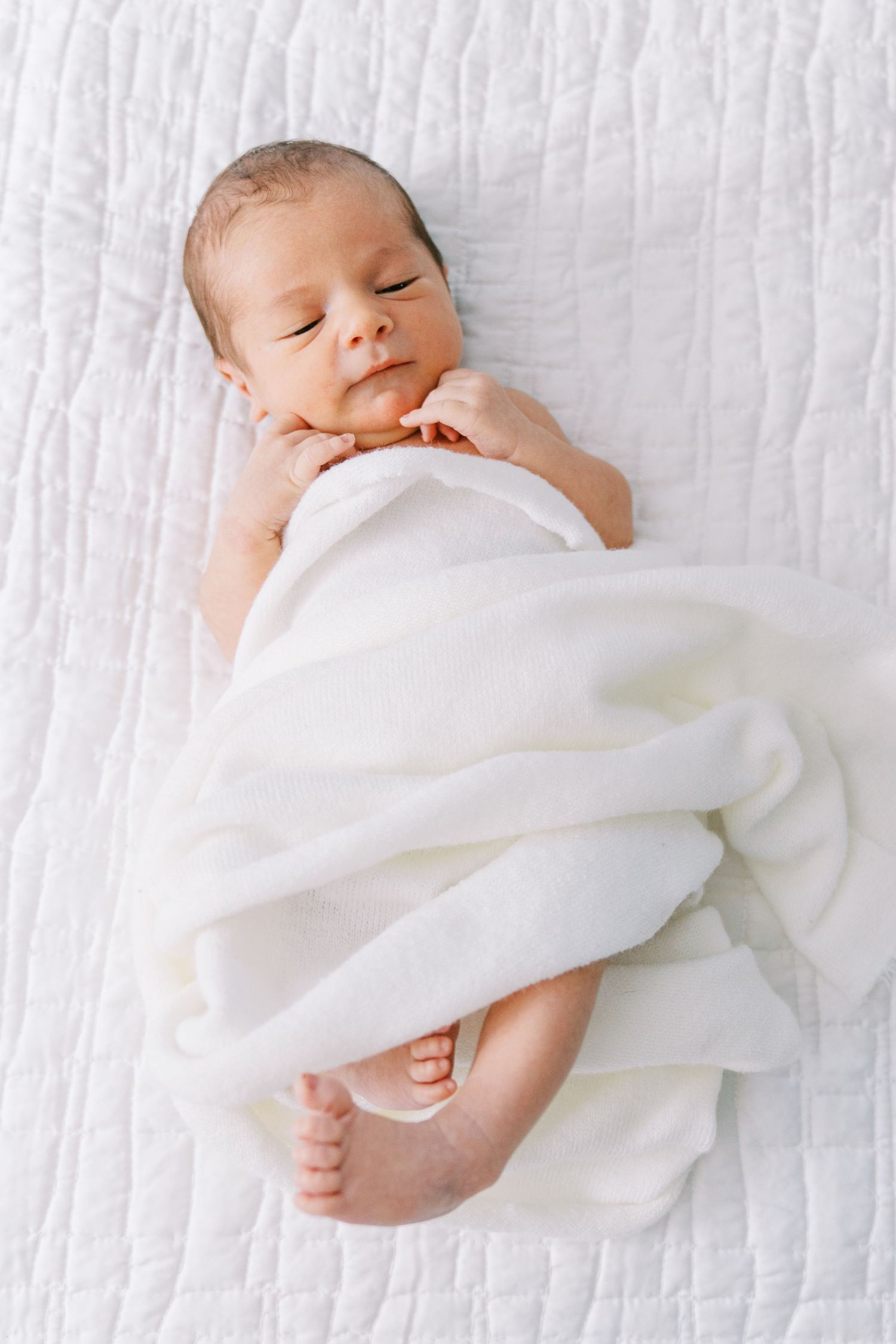 Sleeping newborn baby swaddled in white blanket on textured white background in three similar poses.