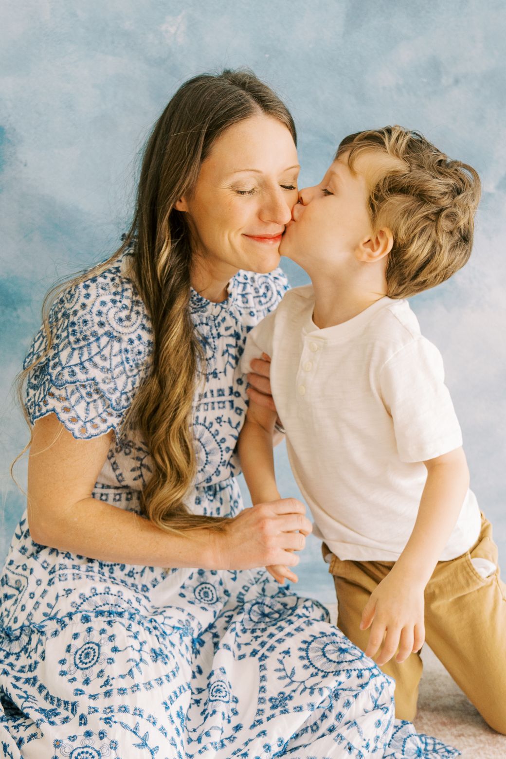 Mother and child share tender moments in matching blue and white outfits against a textured backdrop.