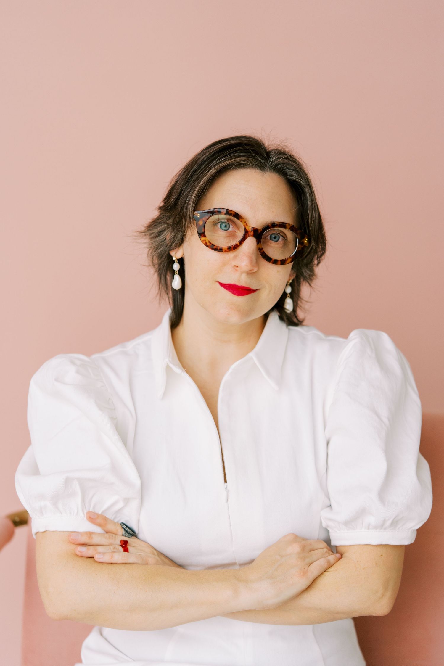 Series of casual headshots against pink backdrop featuring white puff sleeve top and black framed glasses.