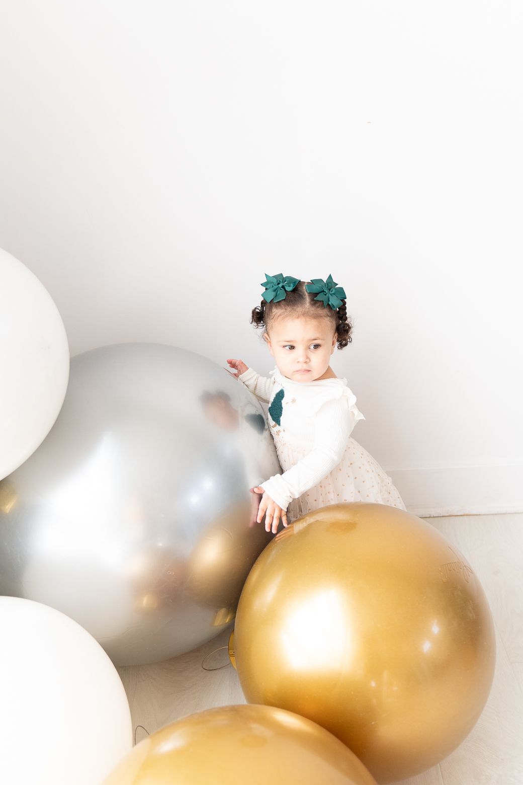 Child playing among large white and gold balloons during a festive holiday photoshoot.