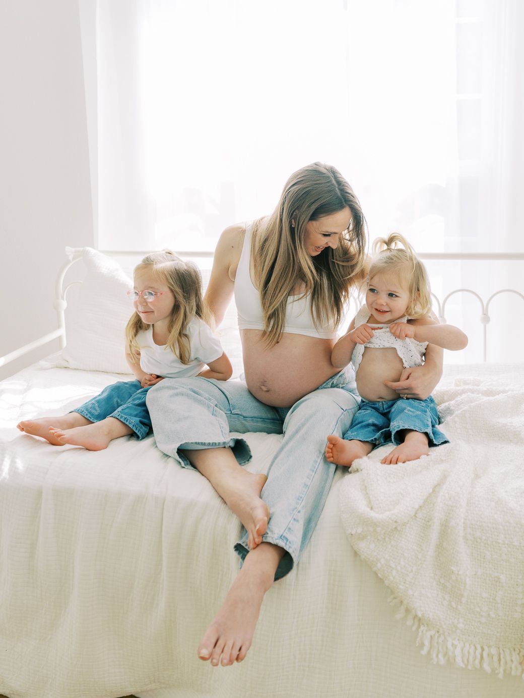 A tender moment captured on a white bed showing affectionate interaction between parent and child in soft lighting.