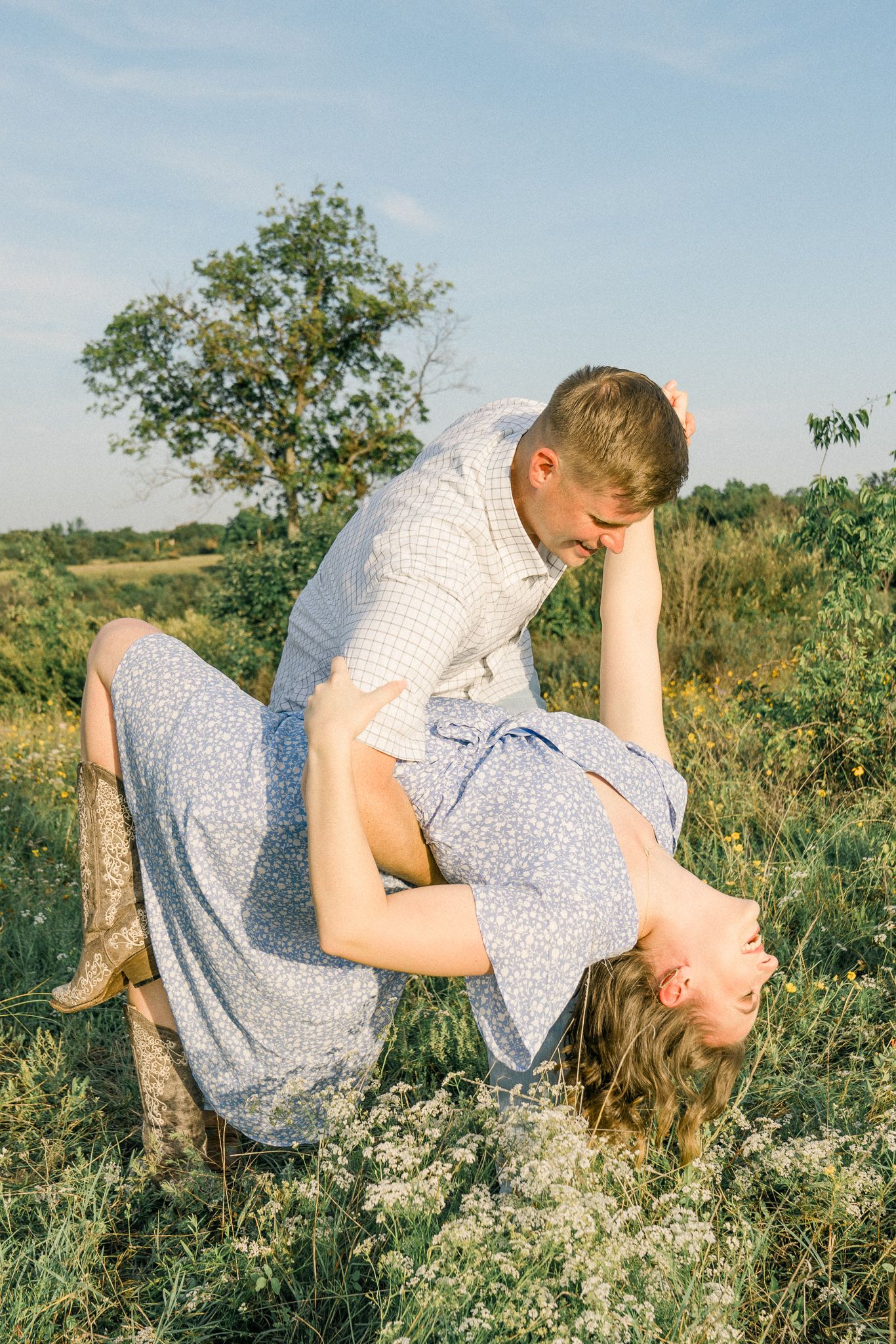 A couple embraces in a romantic moment while sitting in a grassy field on a sunny day.