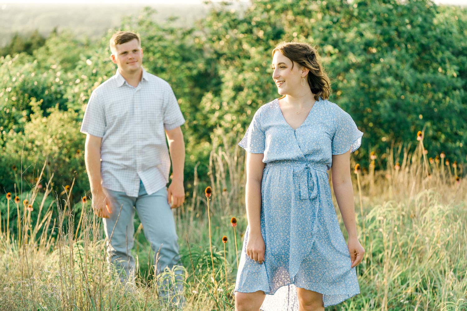 Couple in matching light blue attire walks hand in hand through a blooming meadow on a sunny afternoon.