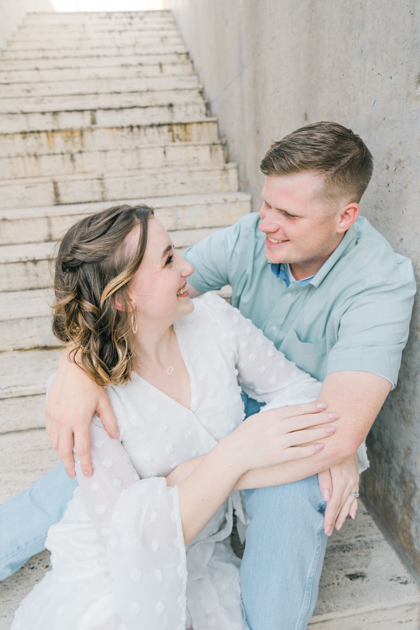 Couple in light blue and white outfits sharing intimate moments against a rustic brick wall.