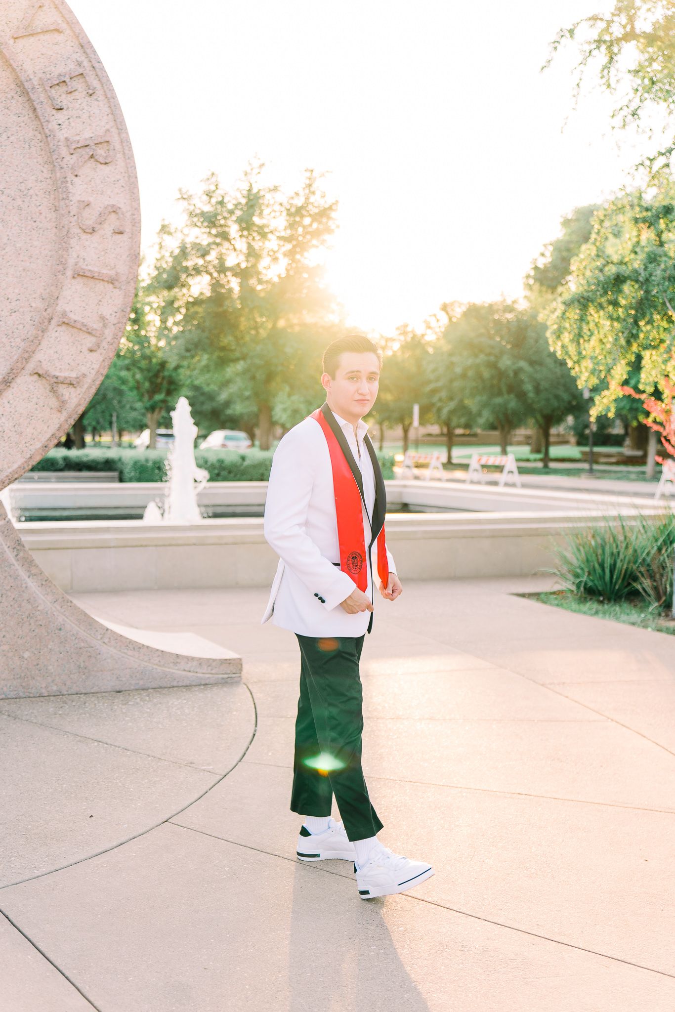 A person in formal attire with red accents stands in an outdoor plaza during golden hour sunset.