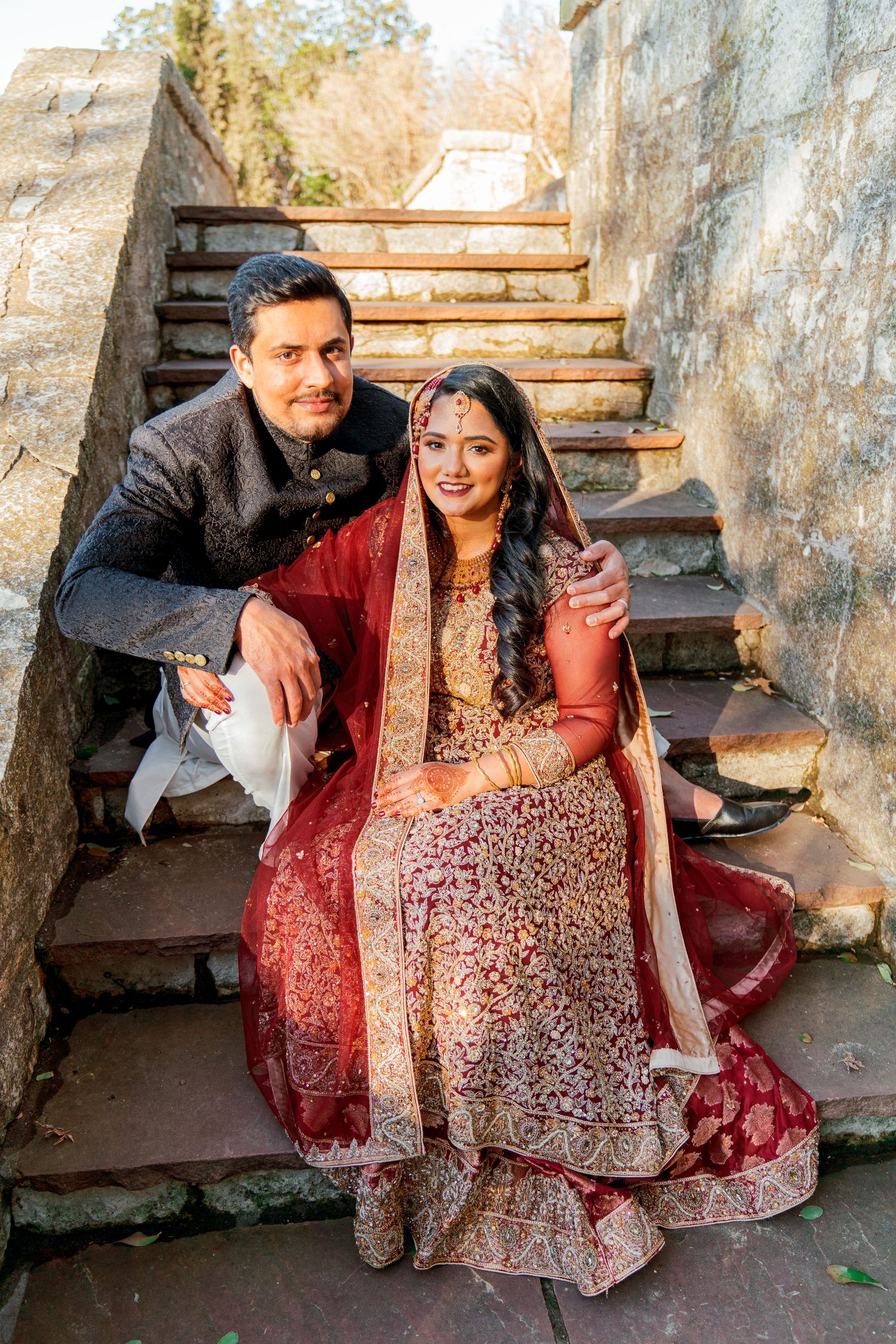 A couple in traditional Indian wedding attire poses on stone steps during a romantic photoshoot.