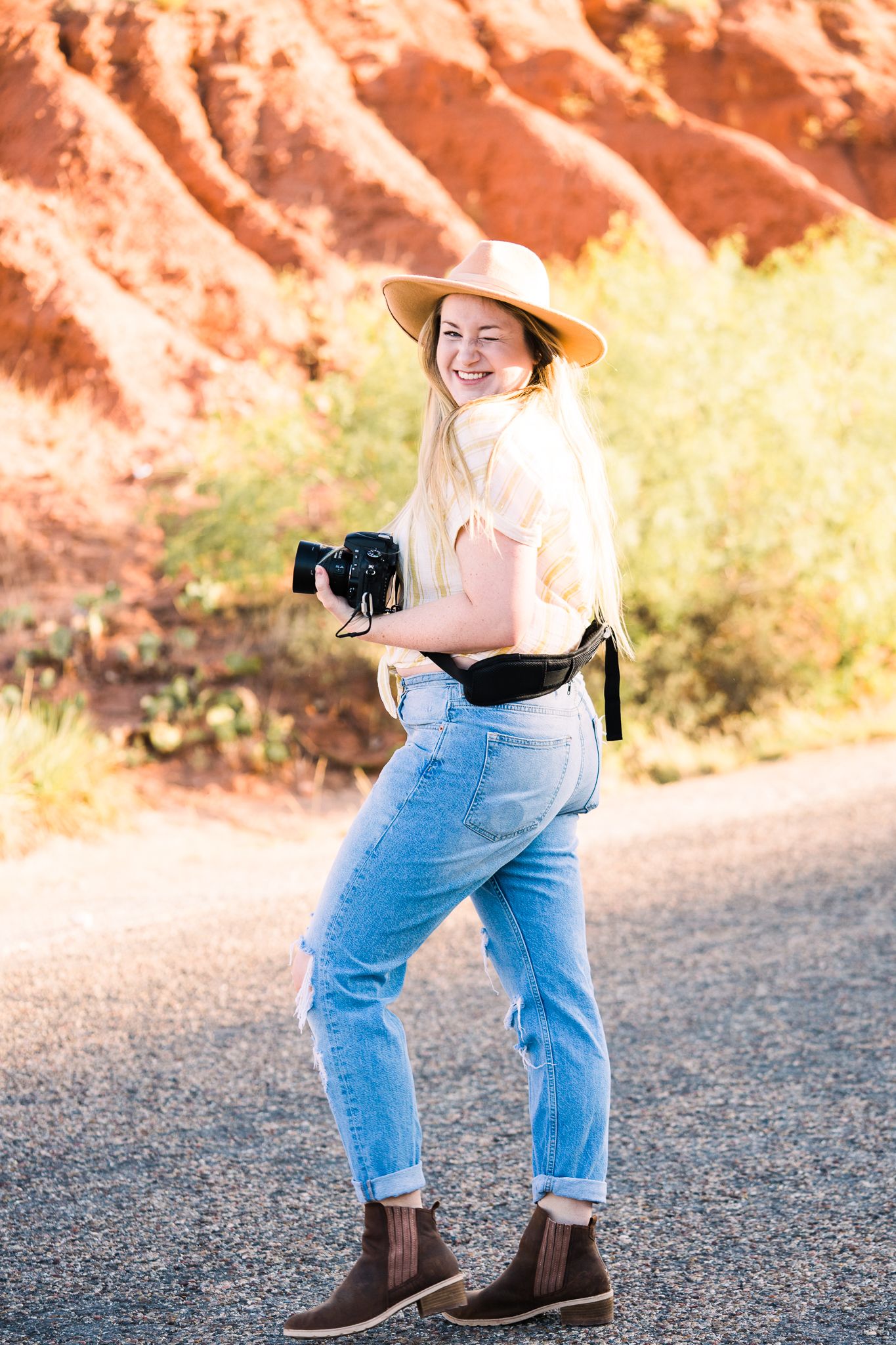 Casual outdoor photoshoot on a desert path with someone wearing boots, distressed jeans and a floppy hat.