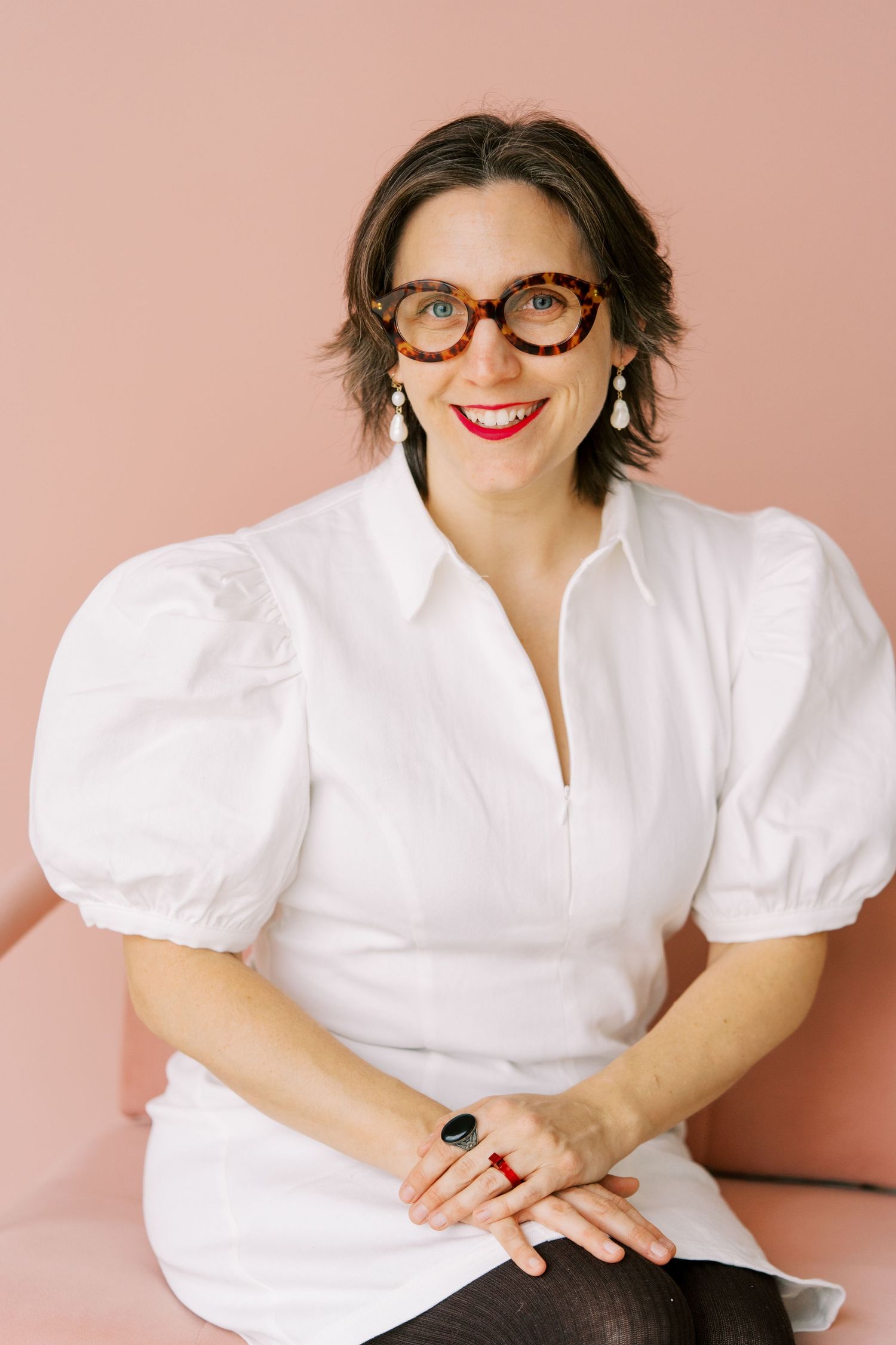 Professional portrait series against pink background showing person in white blouse and red glasses with playful expressions.
