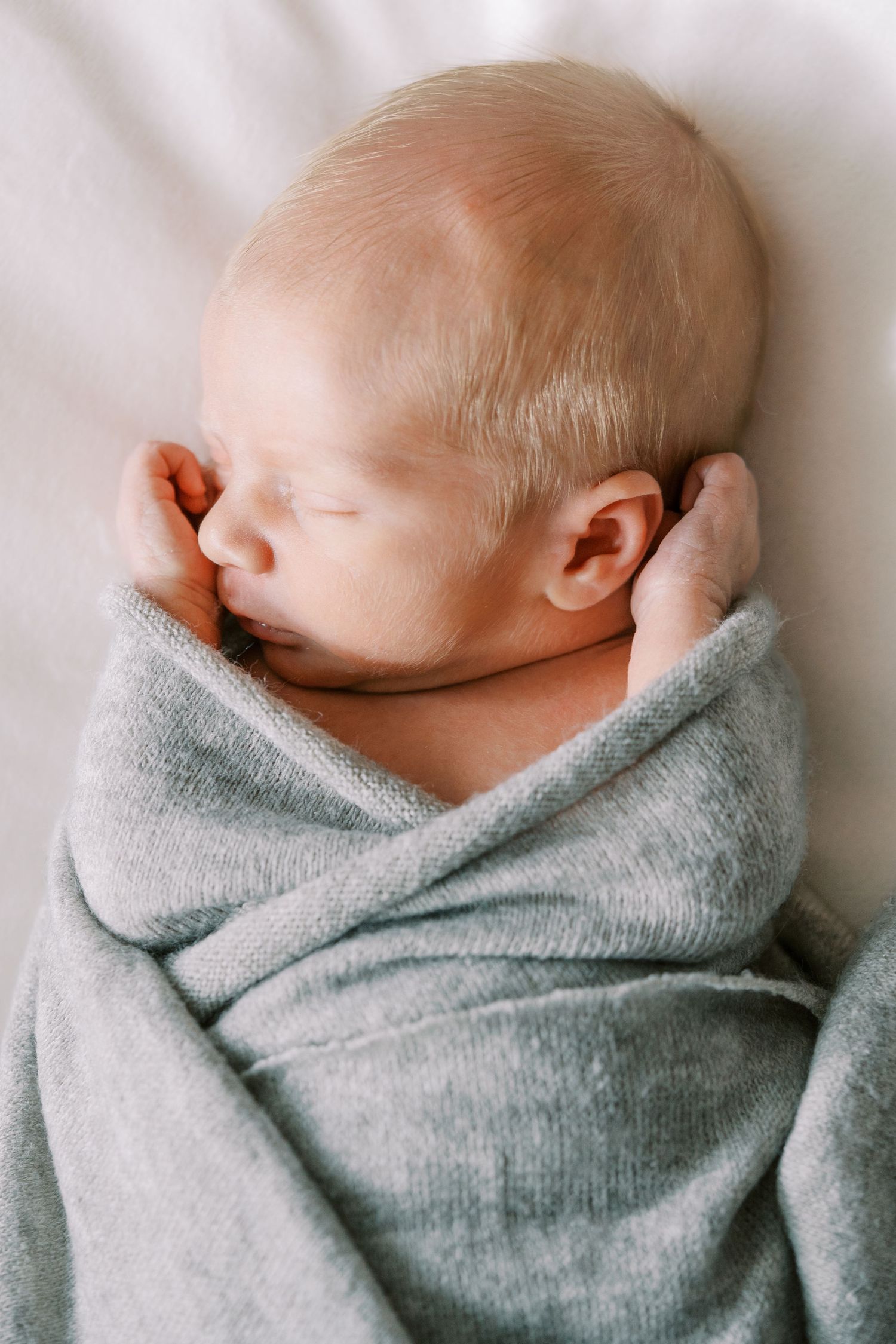 Close-up series of newborn baby swaddled in gray blanket against white background.