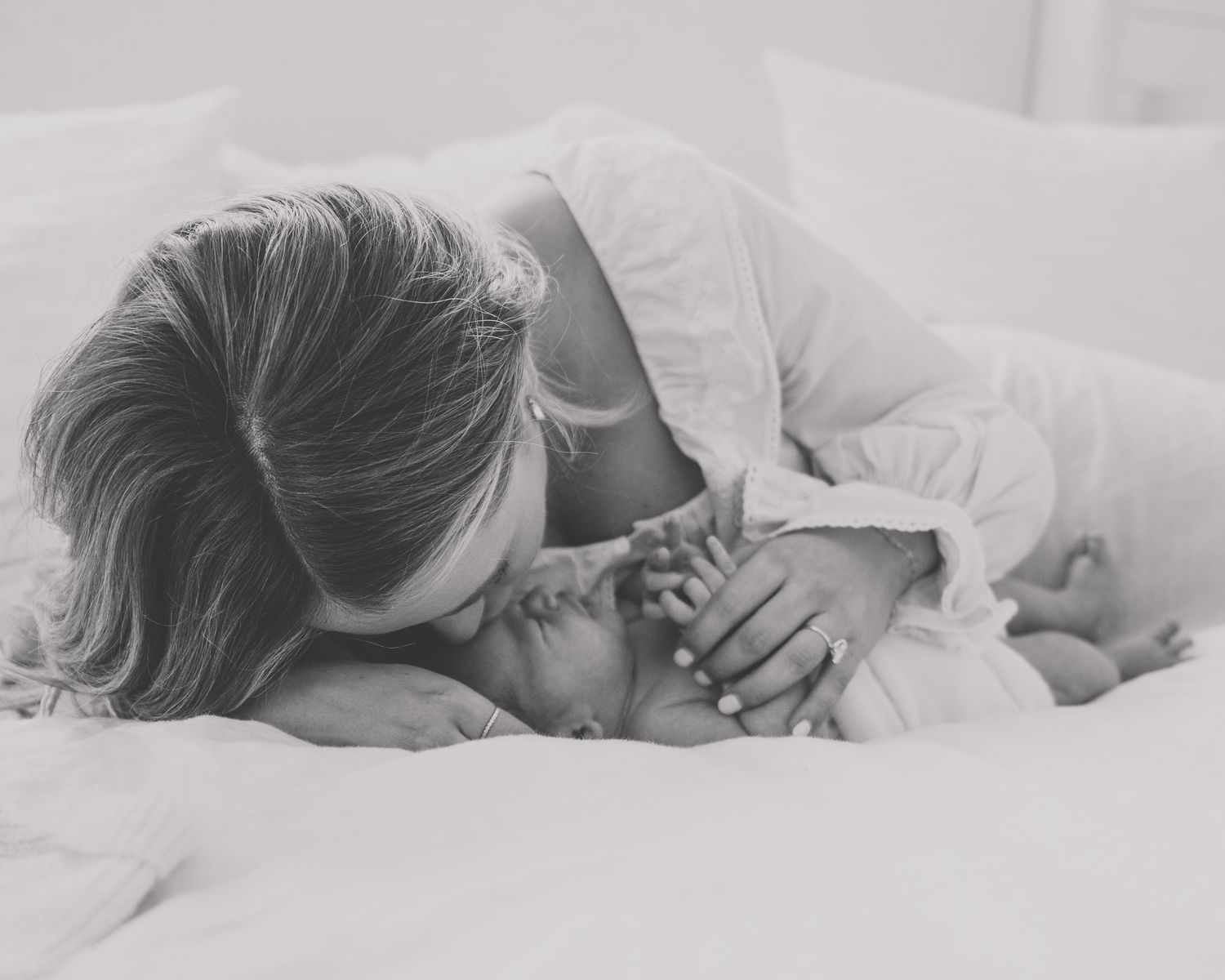 Black and white intimate portrait of mother and baby sharing loving moment on bed.
