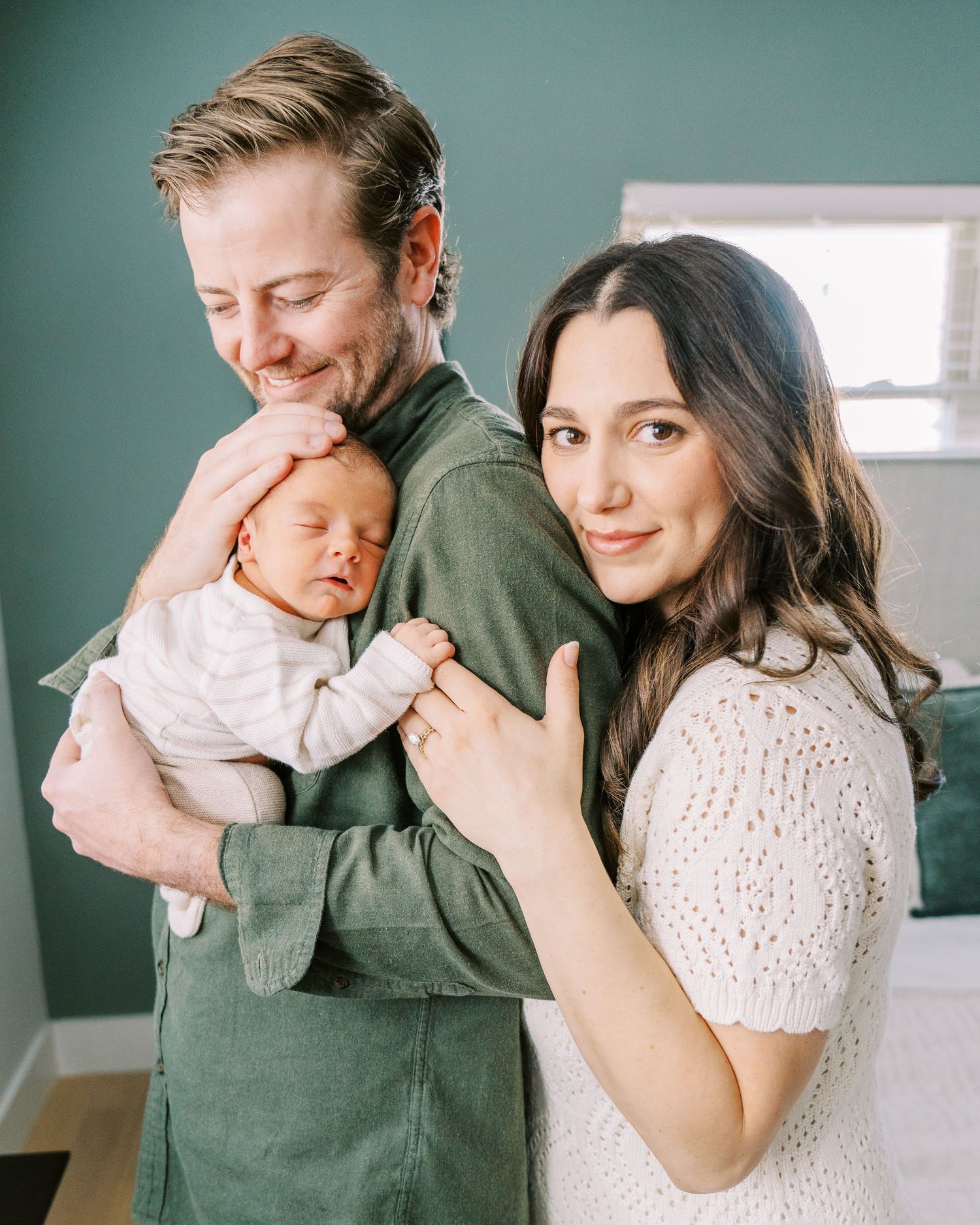 A couple in green and white outfits holds and cuddles with their newborn baby in a series of intimate portraits.