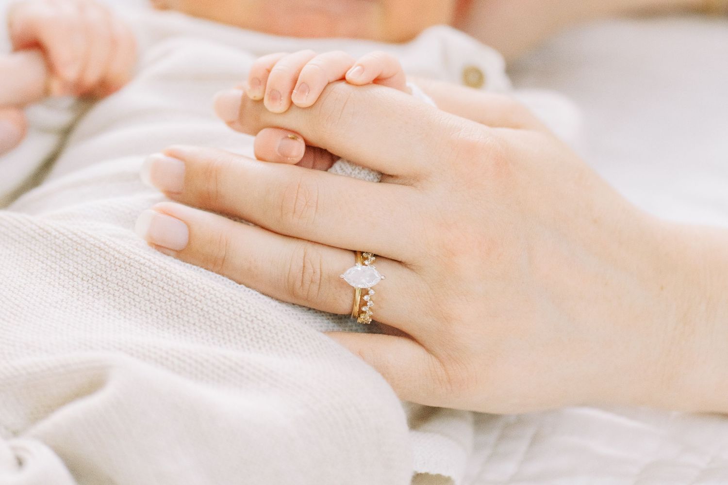 Close-up view of hands wearing engagement ring against white fabric background.