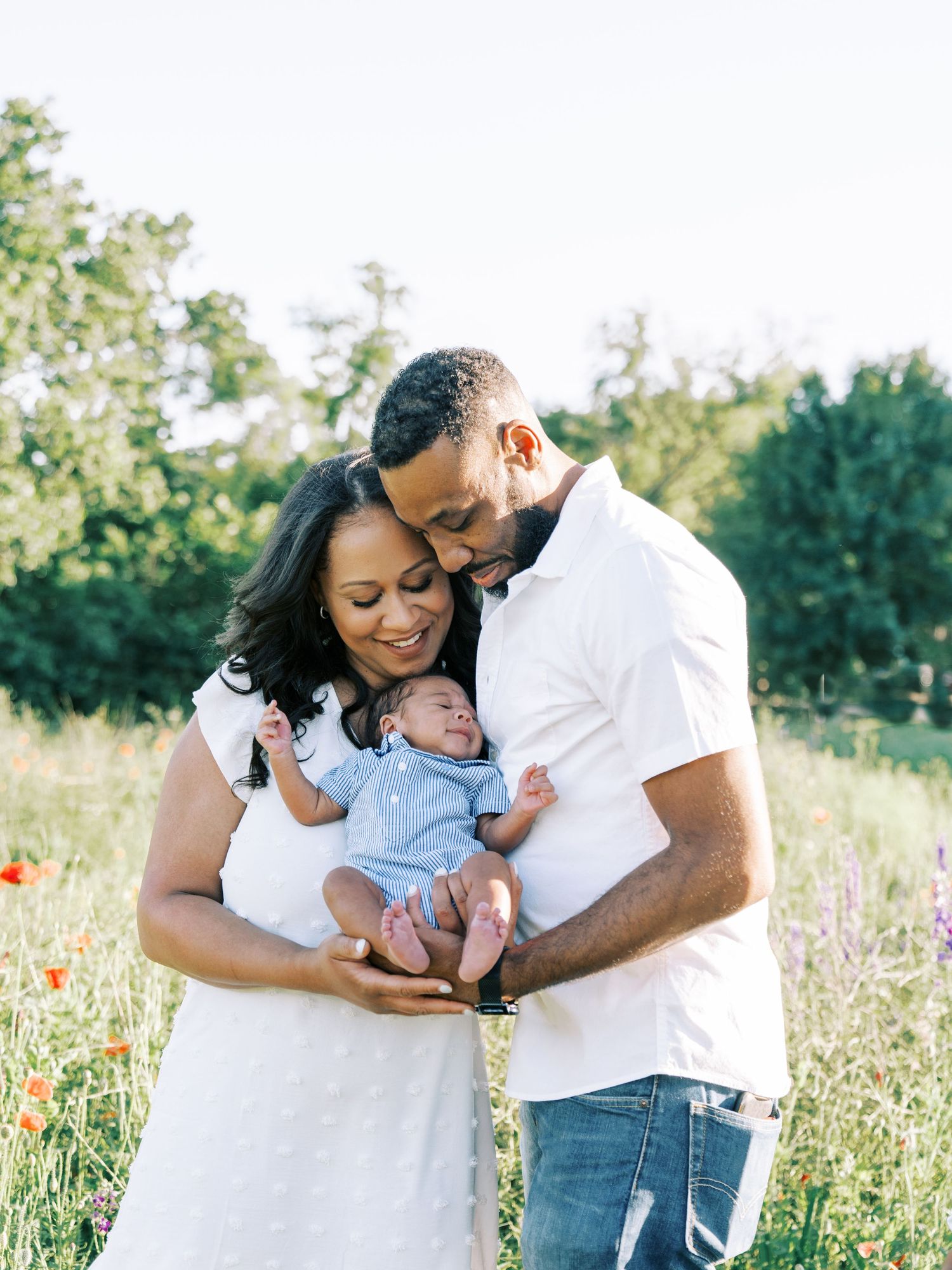 A family shares tender moments together in a sunlit wildflower field wearing coordinating white outfits.