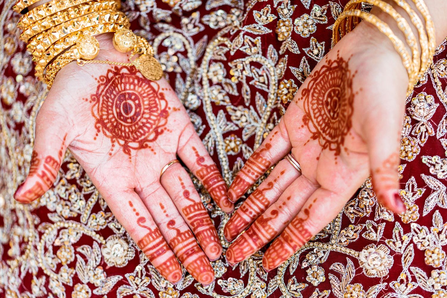 Traditional henna designs displayed on palms against a red and gold background.