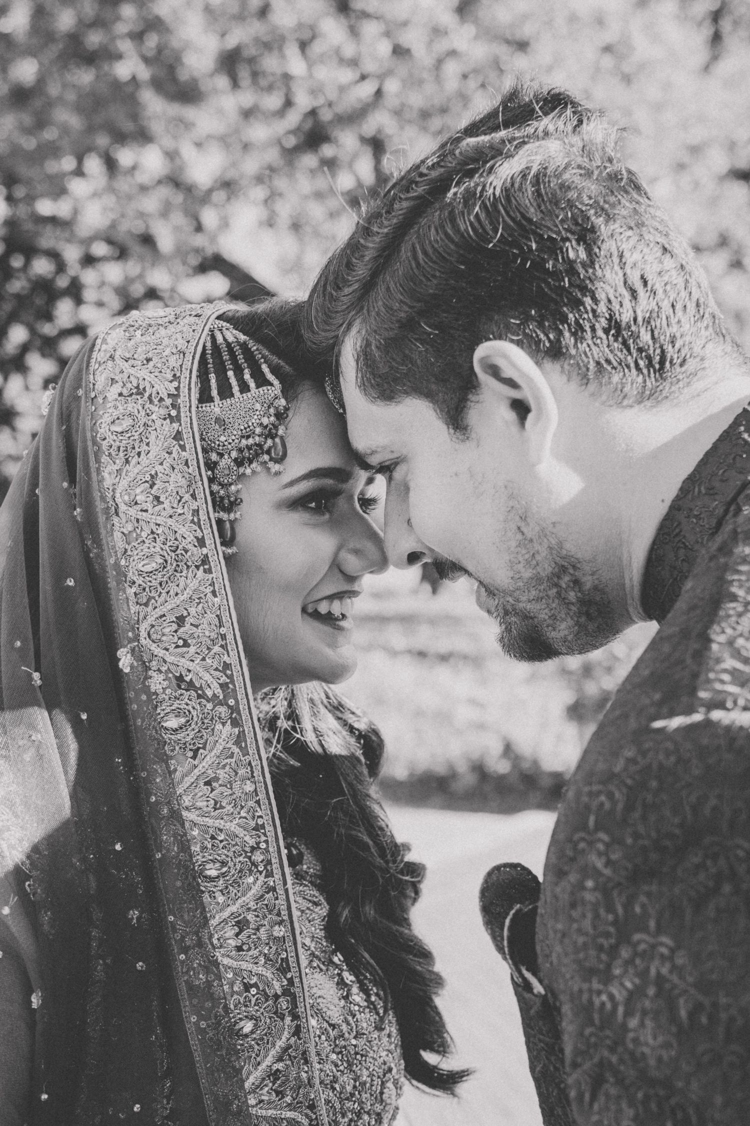 Black and white photo of a couple in traditional wedding attire sharing a tender moment.