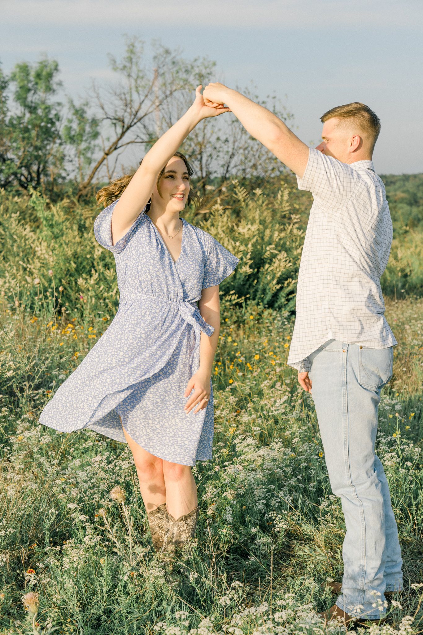 A couple dances together in a wildflower field wearing casual summer attire.
