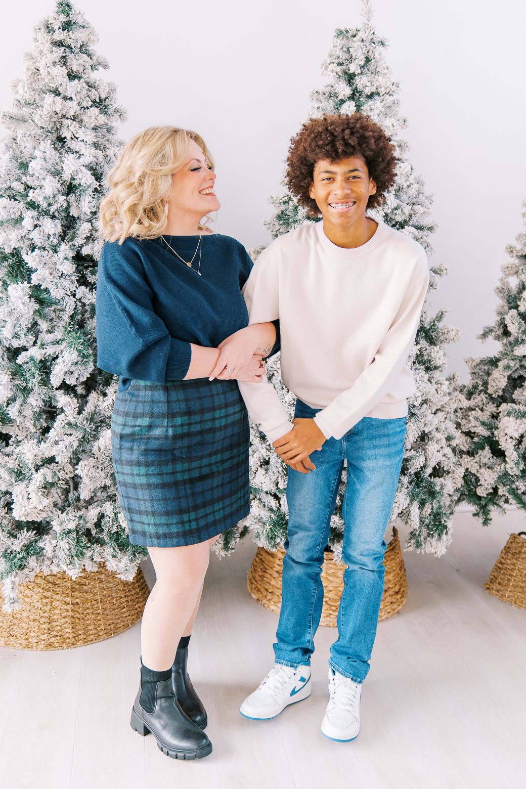 People in casual winter outfits interact playfully in front of snowy white Christmas trees.
