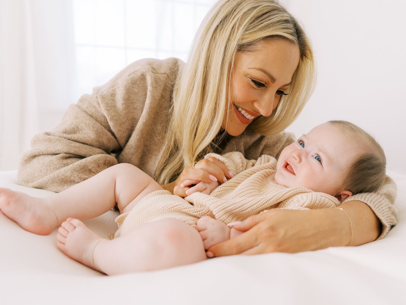 Parent and infant bonding during intimate playtime on white bedding.