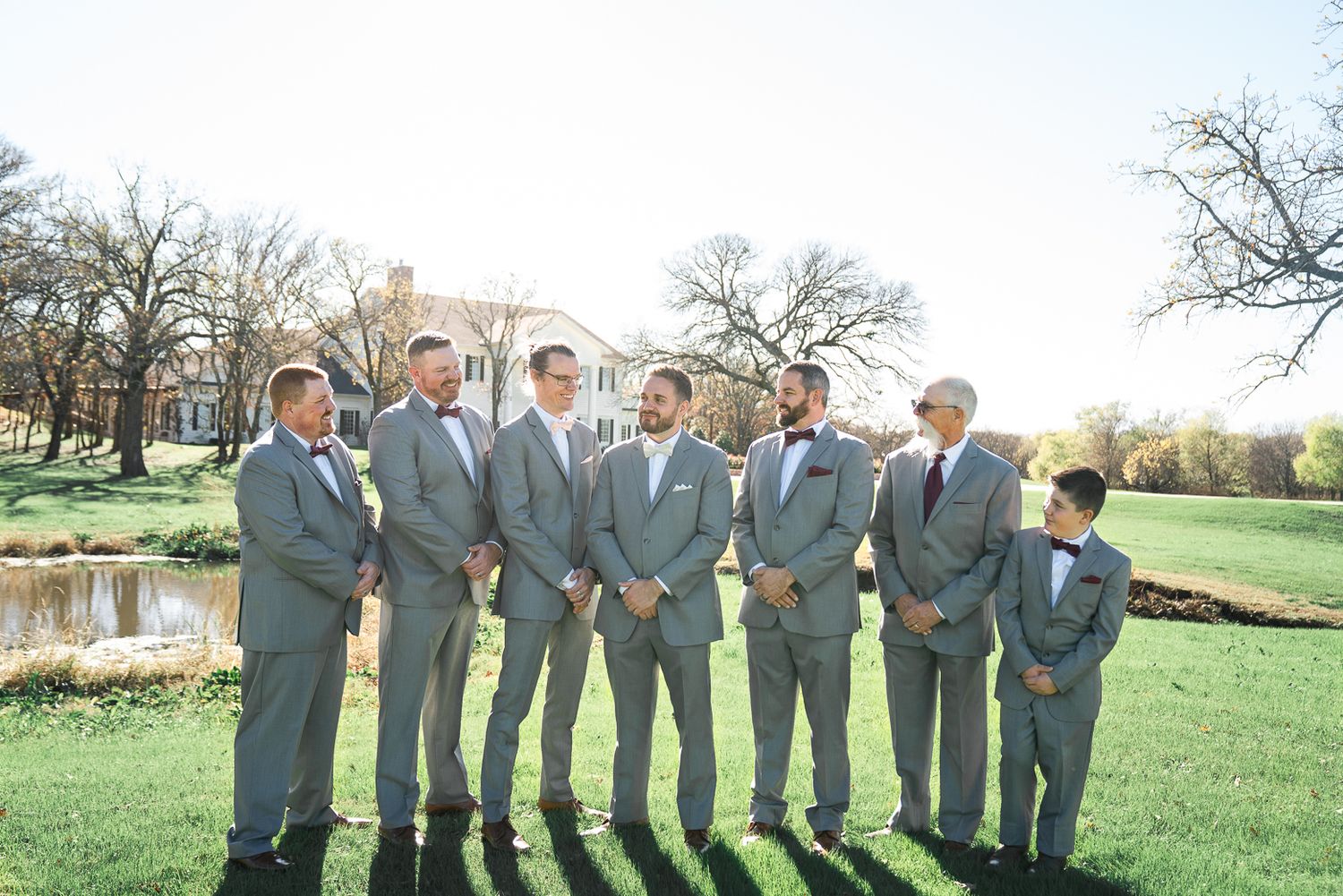 Wedding party in gray suits standing together on a grassy hill during golden hour.
