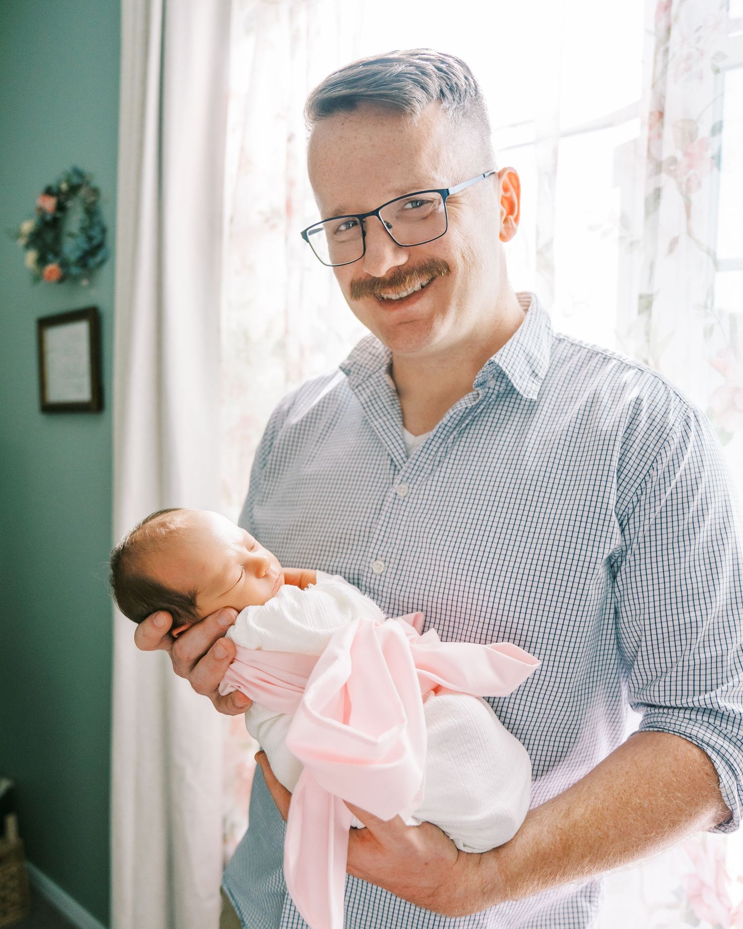 A tender moment as a parent in a checkered shirt holds and gazes lovingly at a baby wrapped in pink.