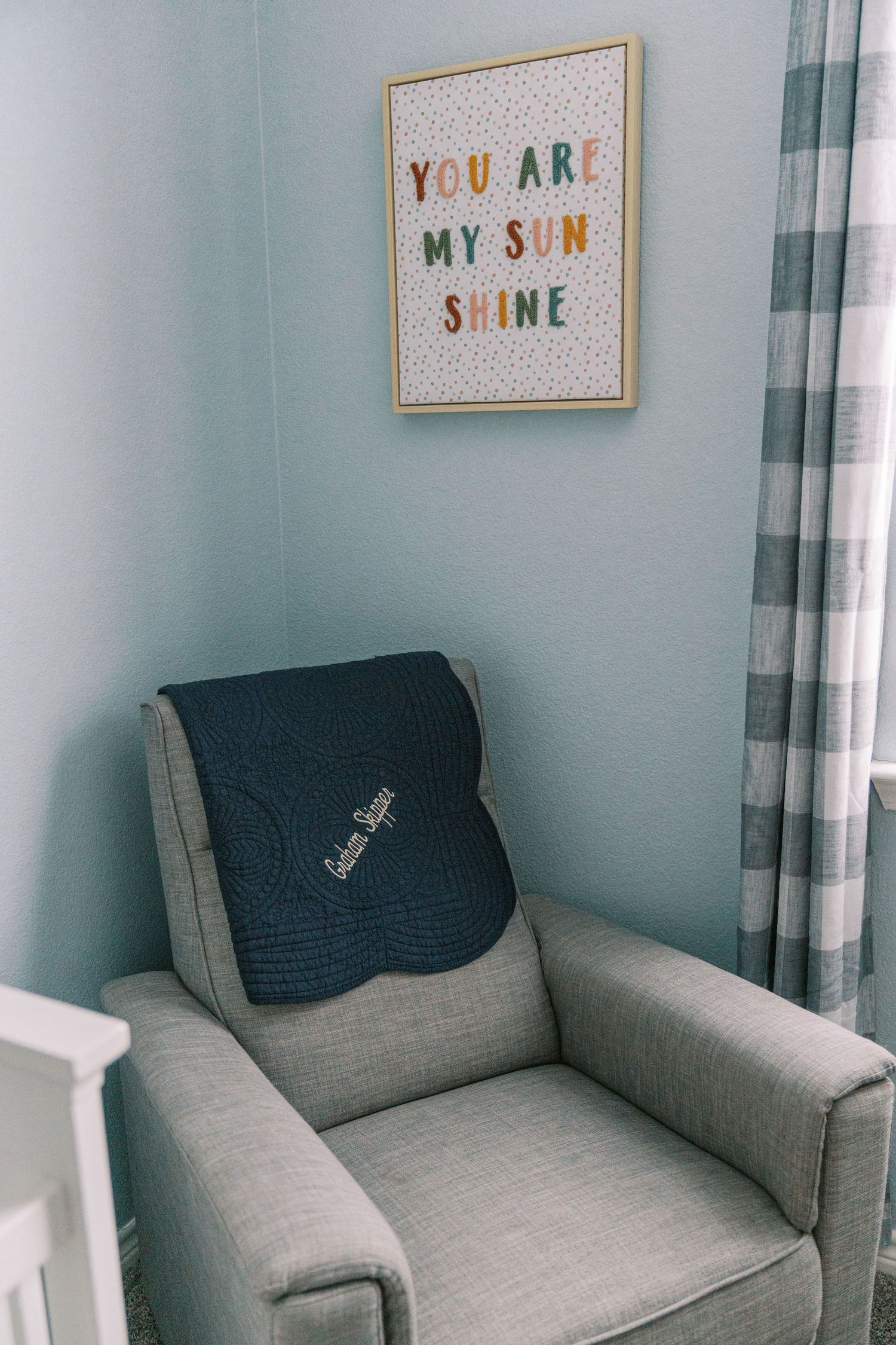 Nursery room with gray armchair and inspirational wall art featuring soft blue walls and white curtains.