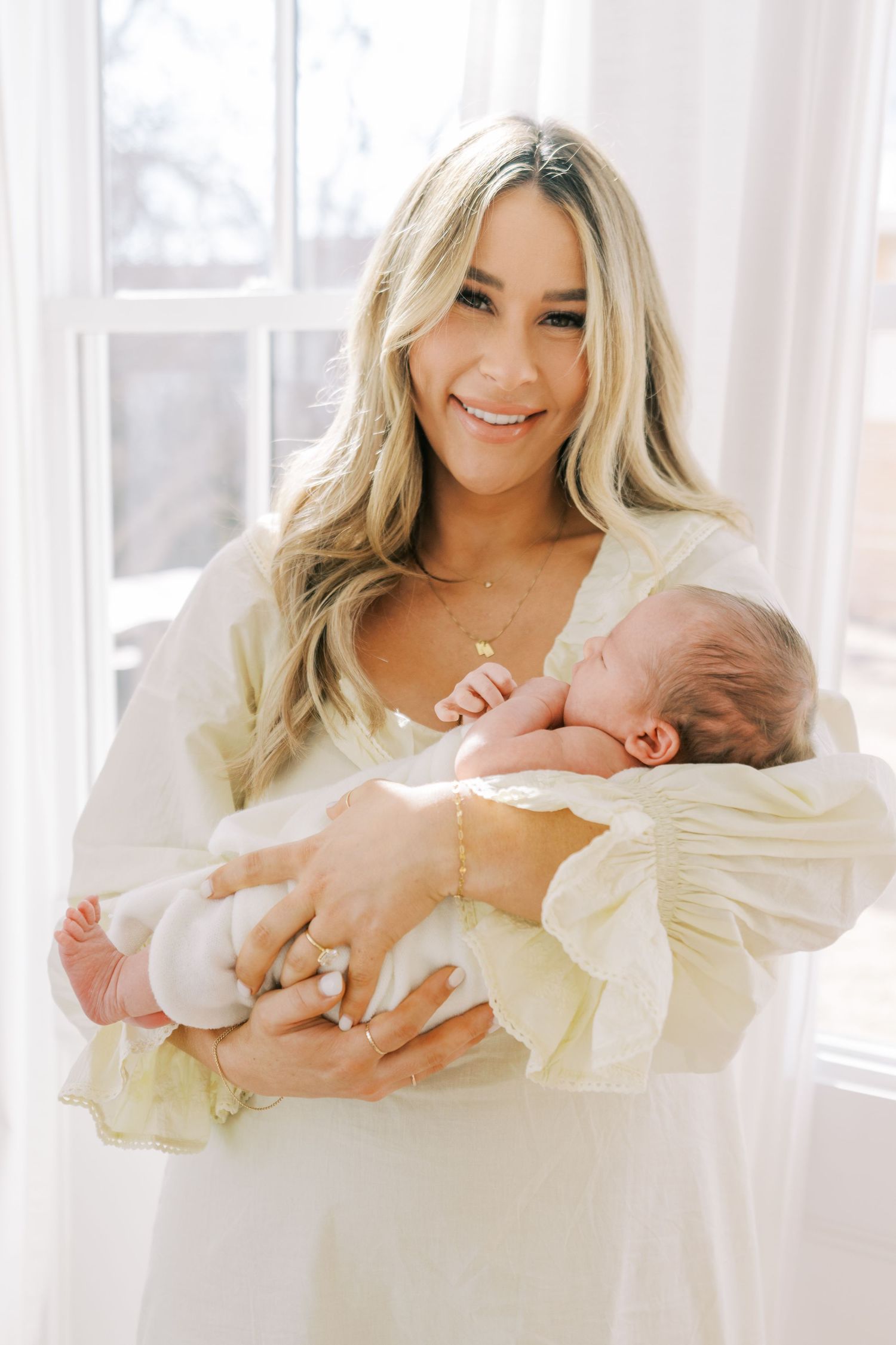 A family in white clothing shares tender moments with their newborn baby in a bright, airy setting.