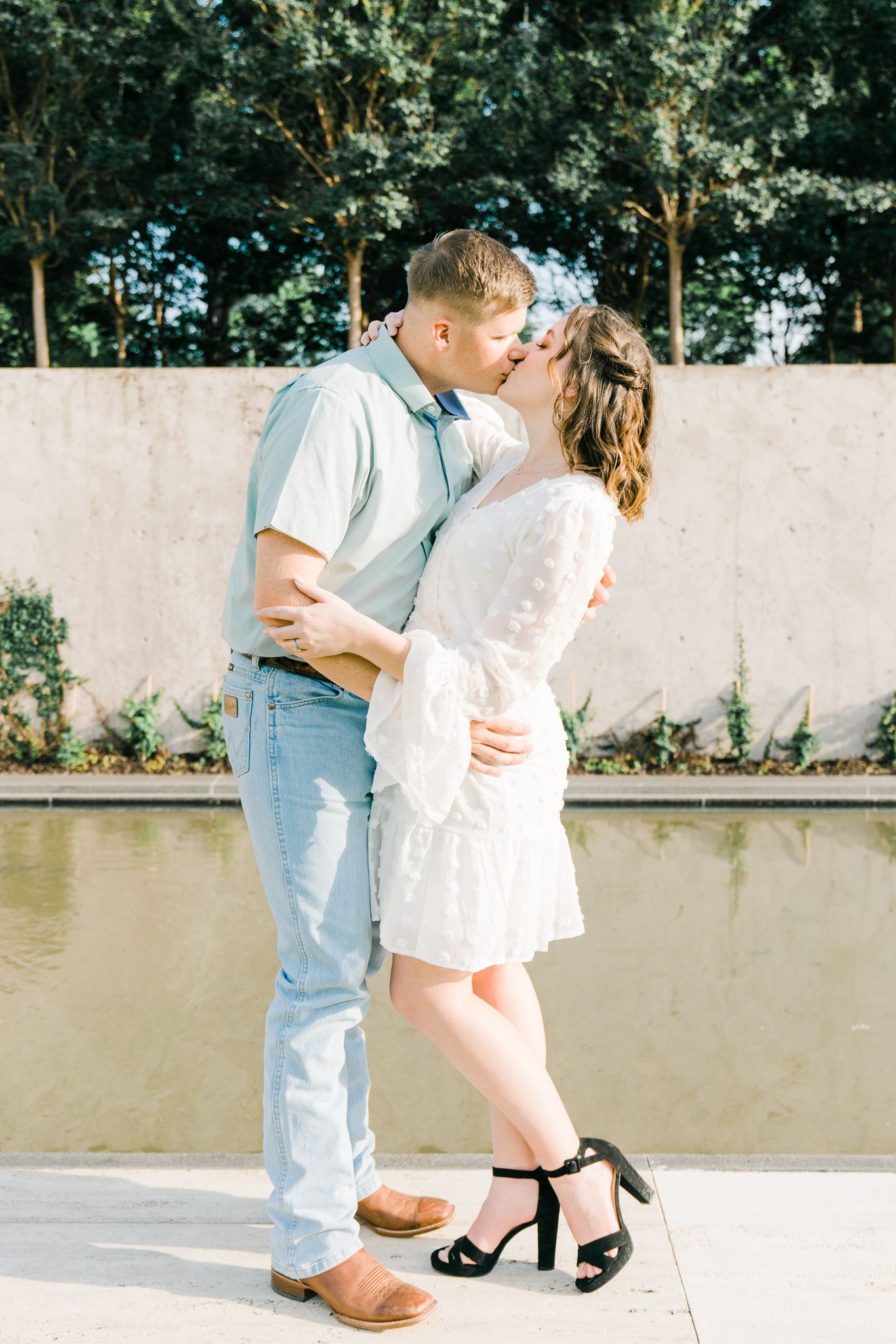 Sweet couple's photoshoot with white dress and denim against a concrete wall backdrop.