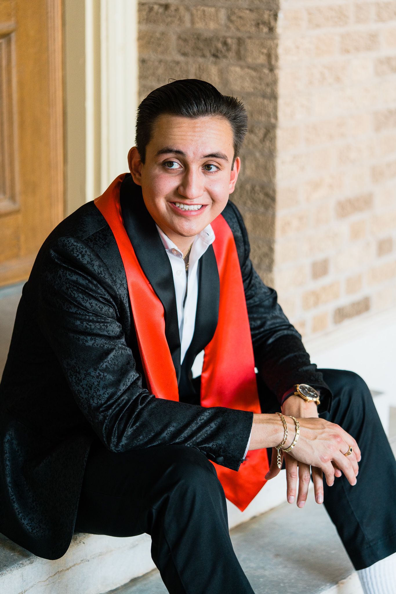 A graduate in black cap and gown with red stole poses for professional portraits against a stone wall.