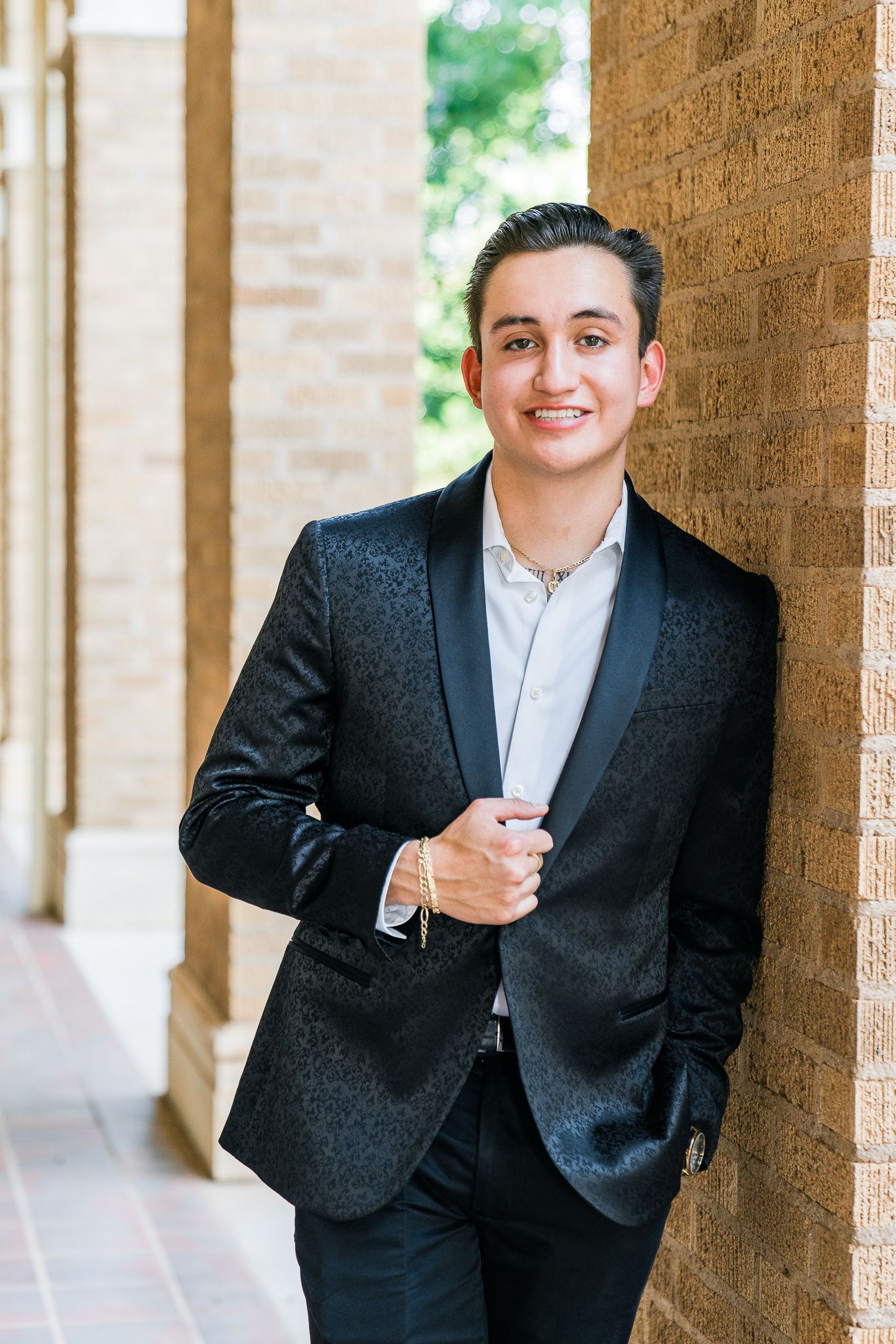 Person in black suit and white shirt smiles while standing in an outdoor brick colonnade.