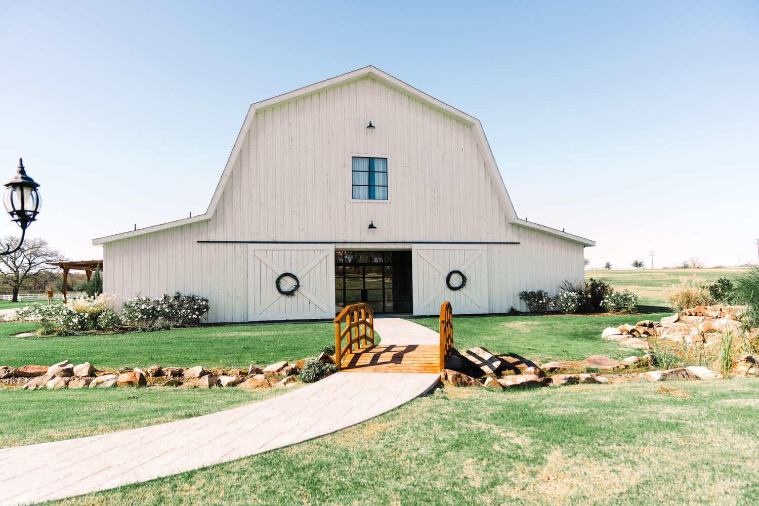 A modern white barn wedding venue with a gambrel roof and decorative circular windows sits on manicured grounds.